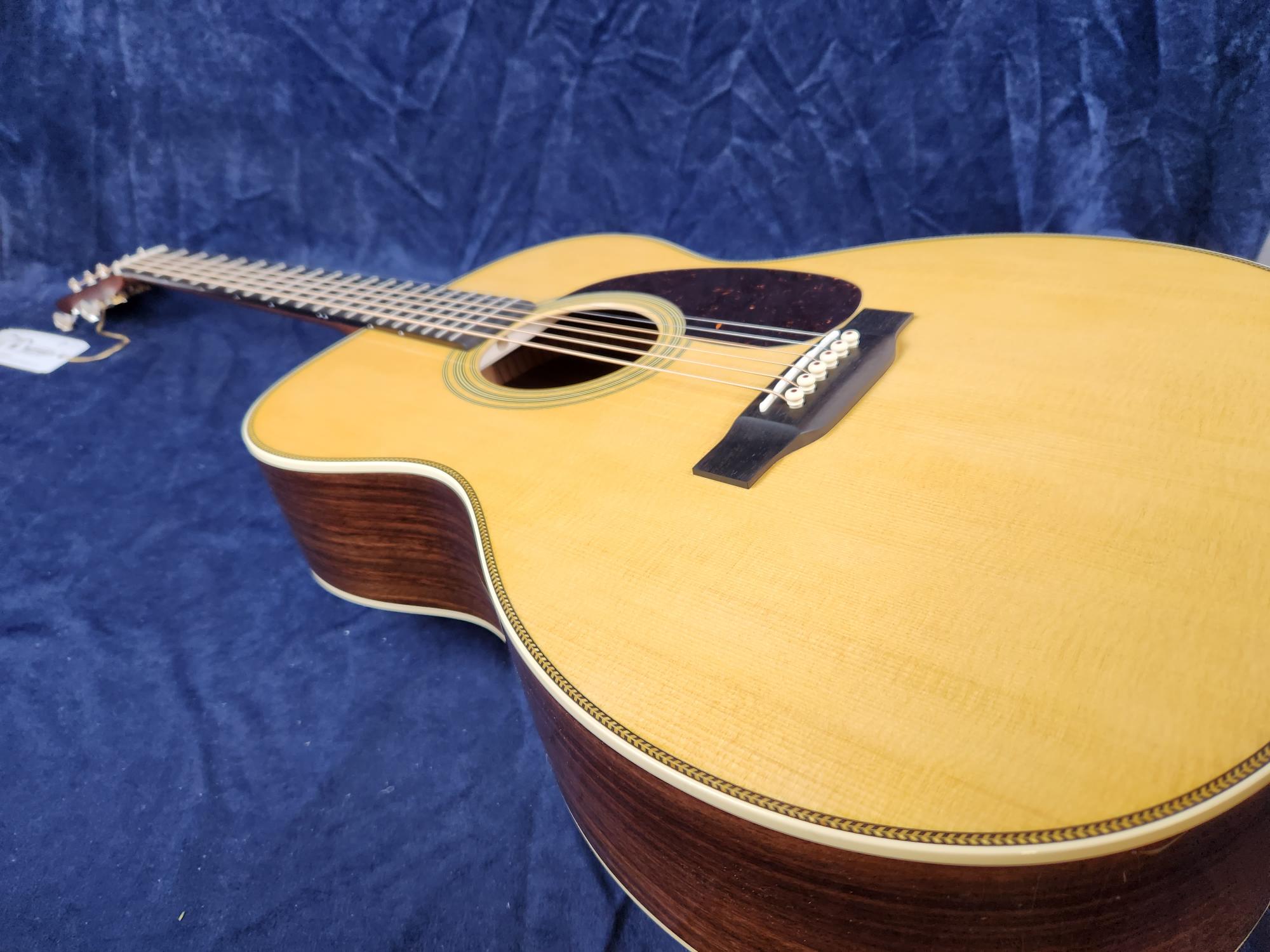 Twelve-string acoustic guitar with a light wood top, dark sides, white binding, and a dark pickguard, resting on a blue fabric background.