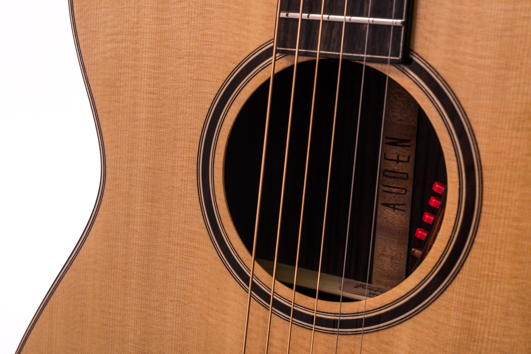 Close-up of an acoustic guitar’s sound hole, with visible strings, wood grain, and red electronics controls inside the body.