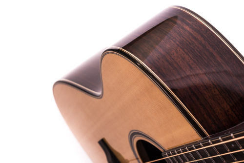 Glossy acoustic guitar with a light wood top, dark wood sides, cutaway body, and visible strings, shown close up from the side.