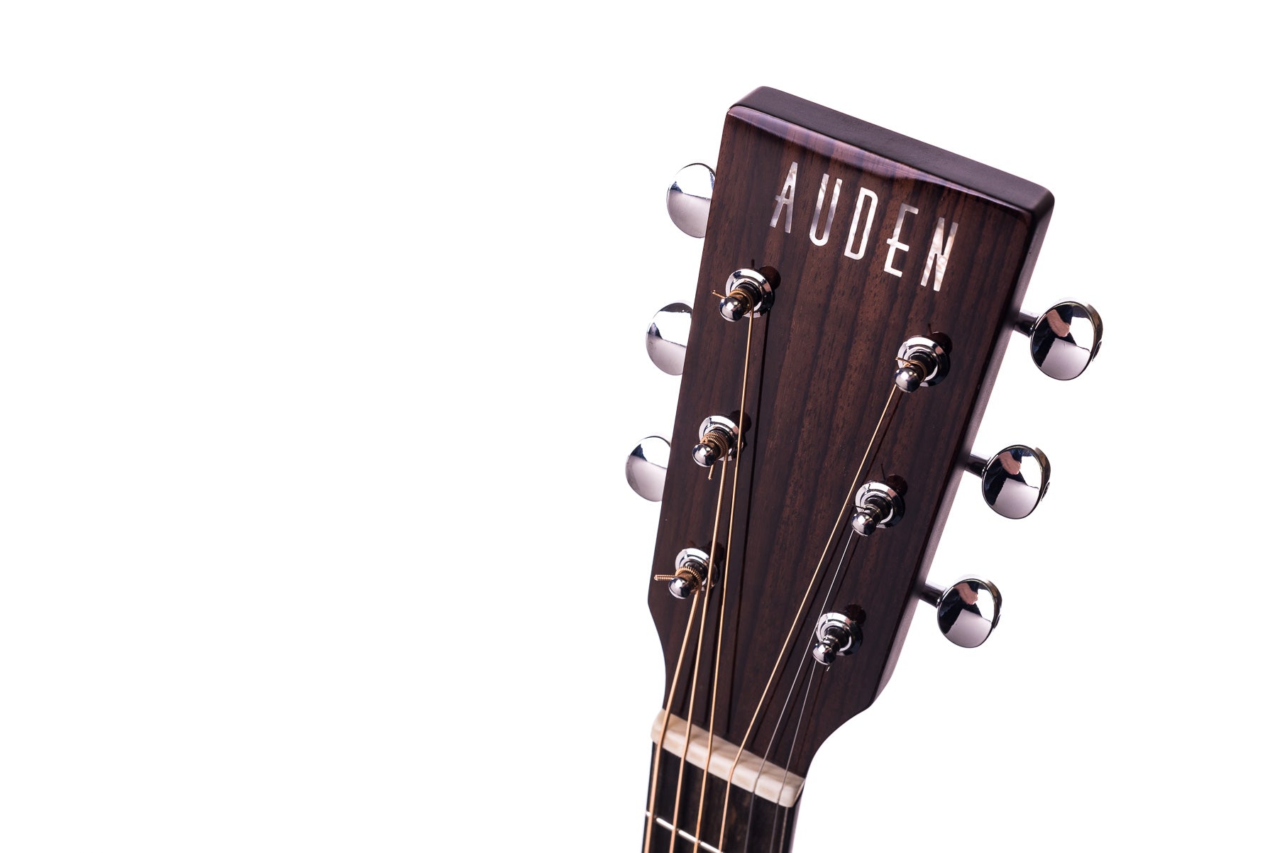 Dark wooden headstock of an Auden acoustic guitar with six chrome tuning pegs and visible metal strings on a white background.