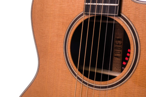 Close-up of an acoustic guitar’s body and soundhole, showing six strings and red control buttons inside the soundhole.
