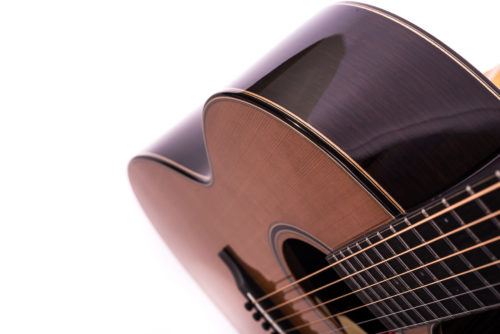 Close-up view of an acoustic guitar showing the glossy dark sides, cutaway body shape, wooden top, and steel strings.