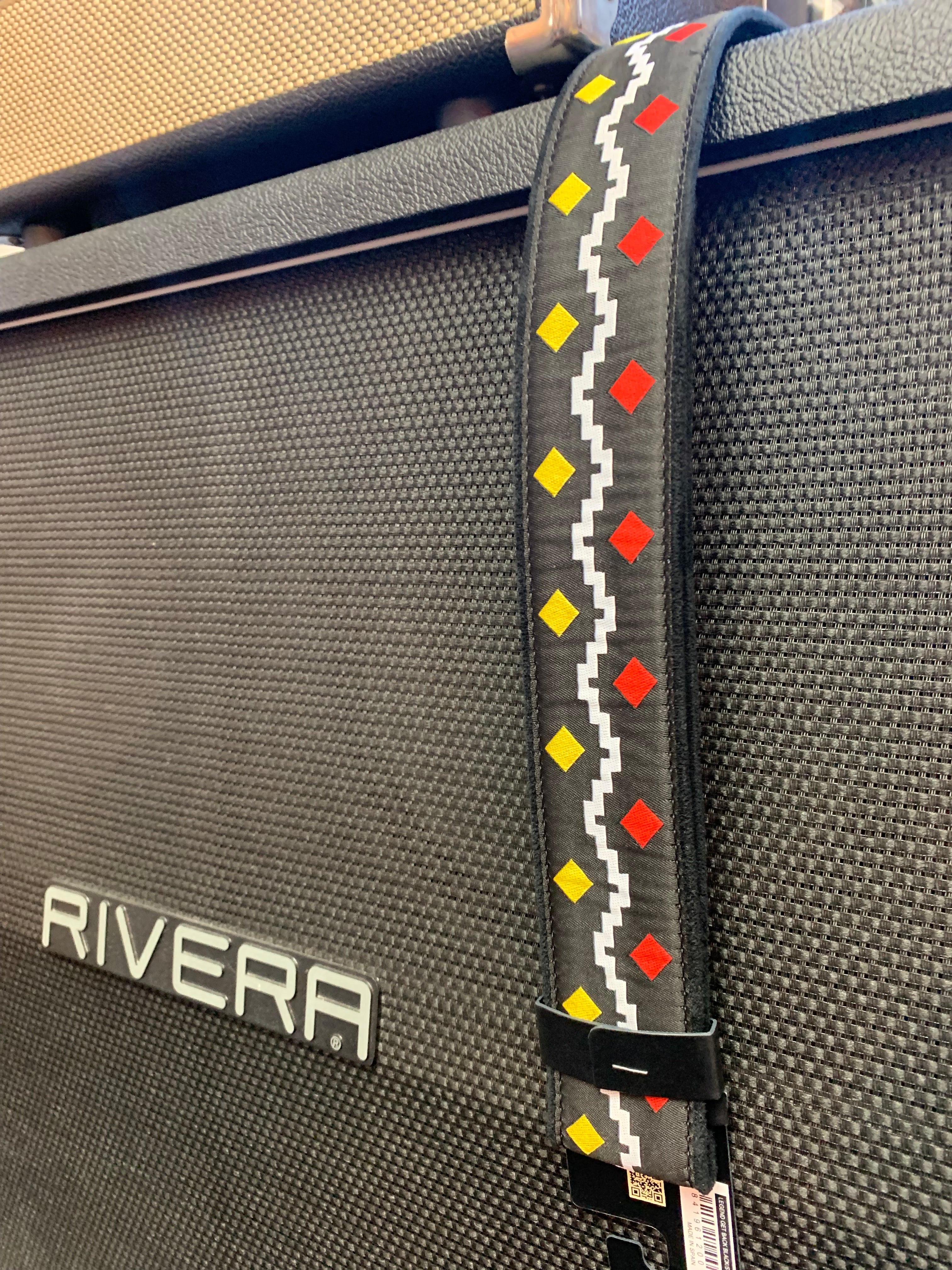 Guitar strap with zigzag white line and alternating red and yellow diamonds, draped over a black textured Rivera amplifier.