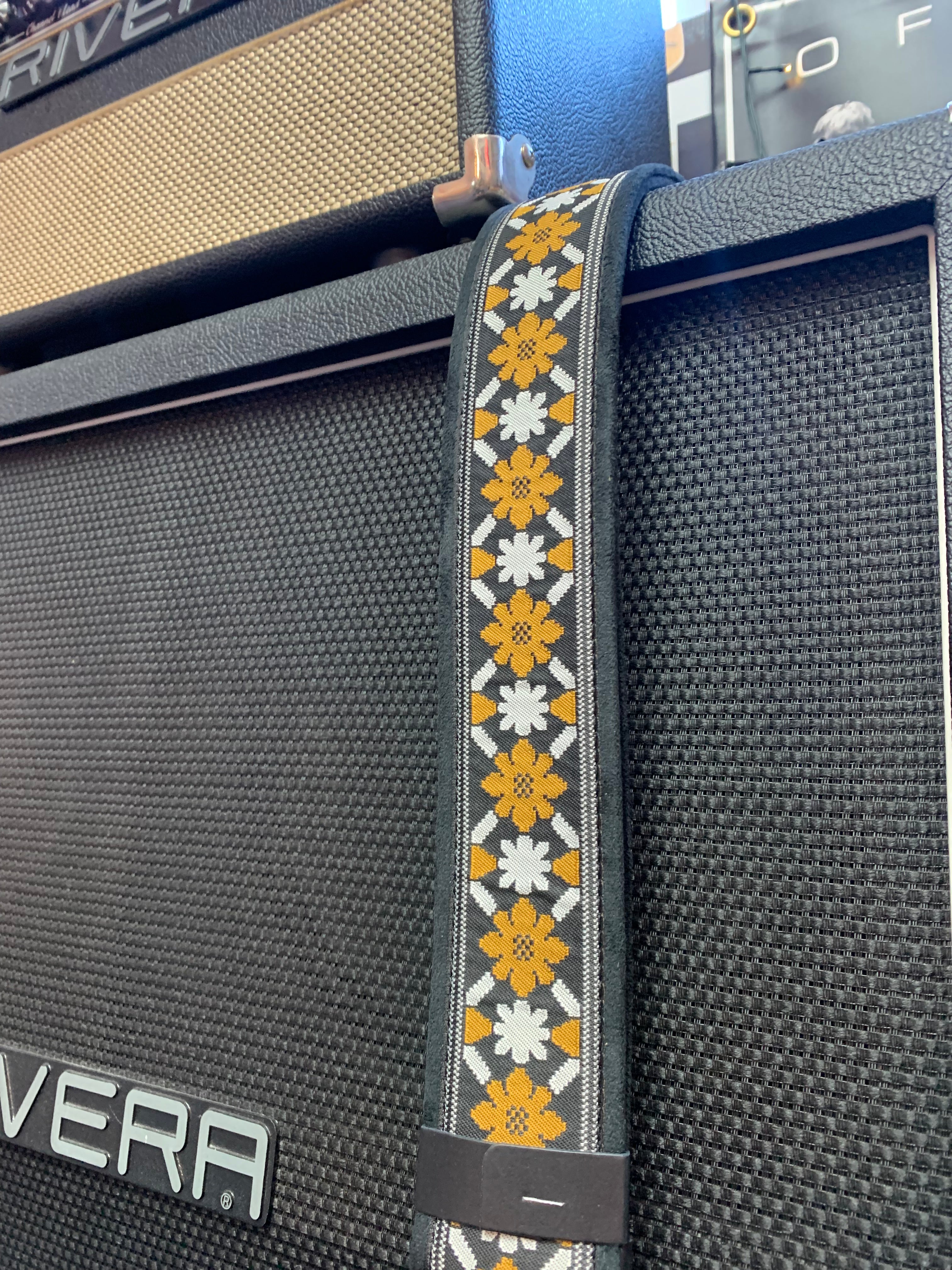 A guitar strap with yellow and white floral patterns hangs over a black Rivera amplifier cabinet.