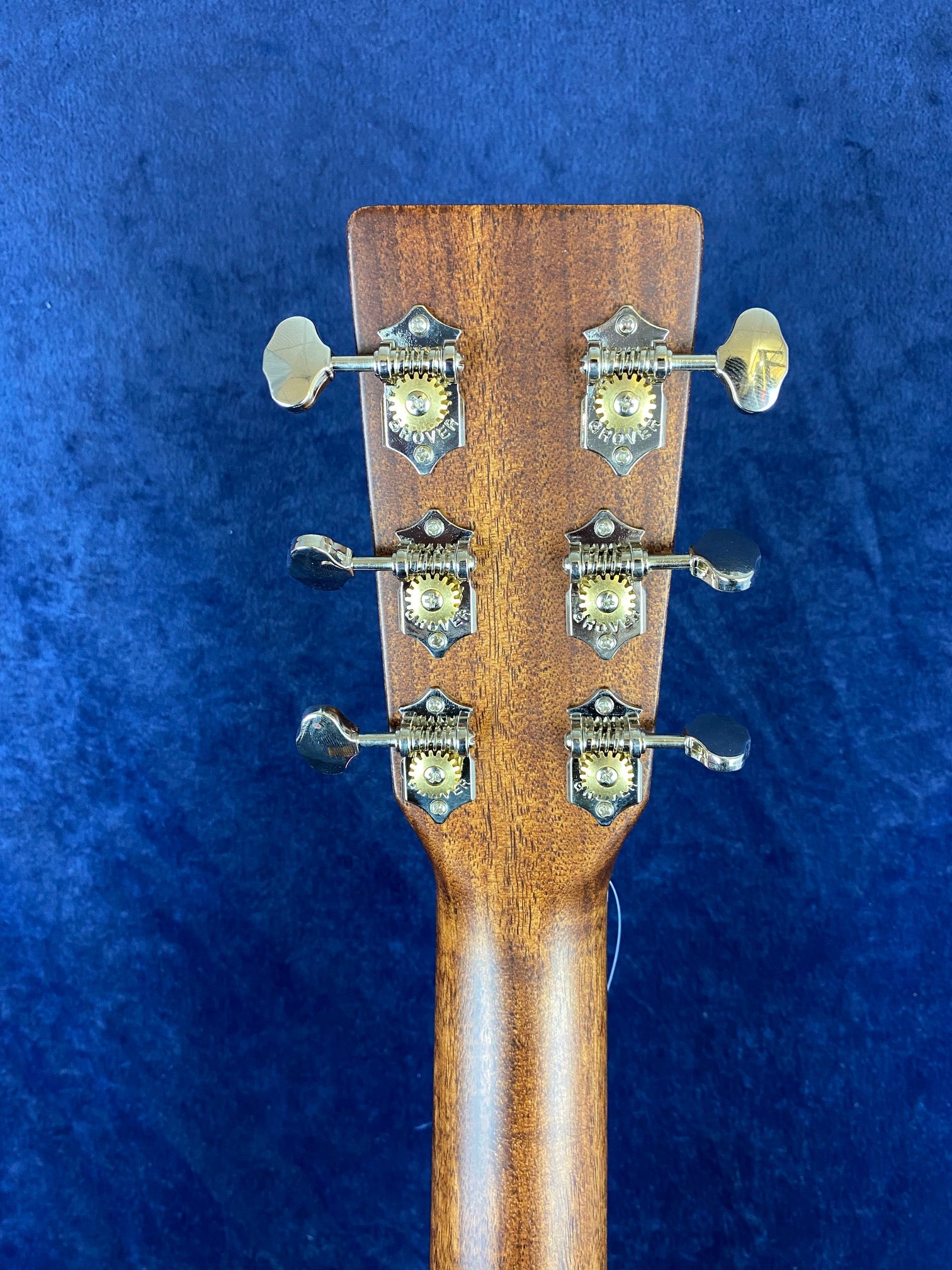 The back of an acoustic guitar’s headstock with six vintage-style Grover tuning pegs, set against a blue velvet background.