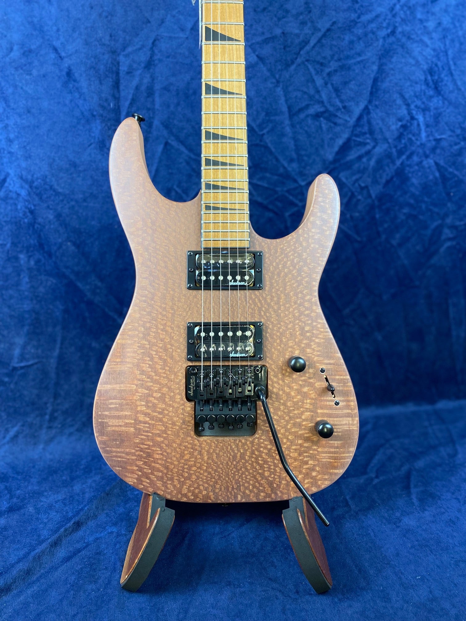 Natural wood finish electric guitar with two black humbucker pickups, a whammy bar, black hardware, and distinct jagged inlays on the fretboard.