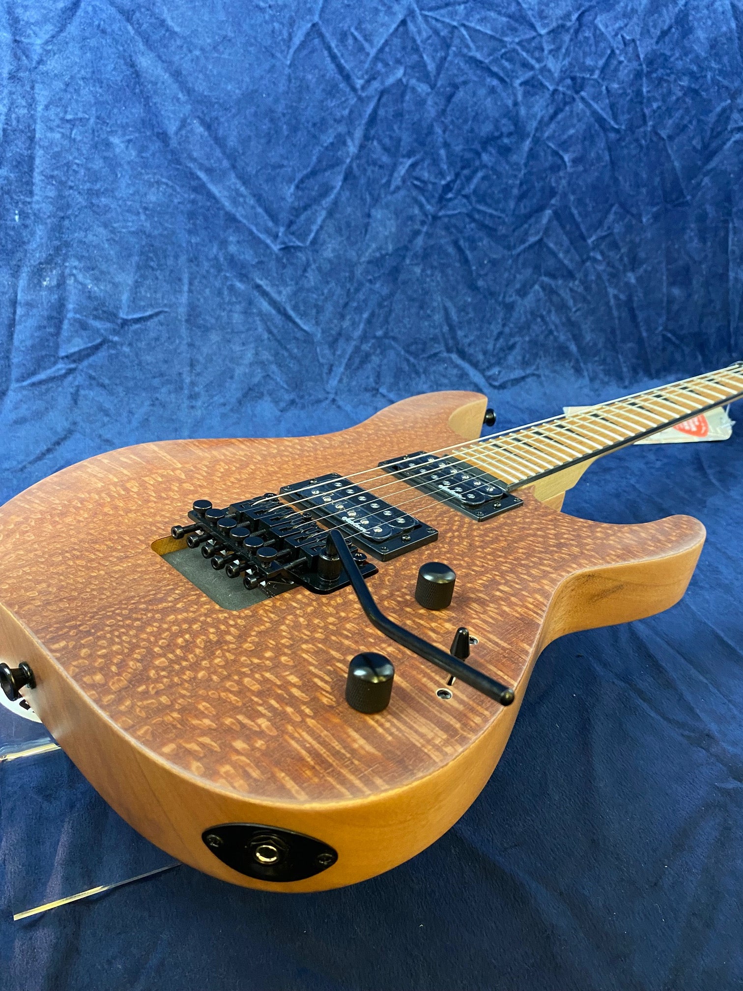 Natural wood finish electric guitar with a textured, spotted top, black humbucker pickups, a tremolo bridge, and two black control knobs.