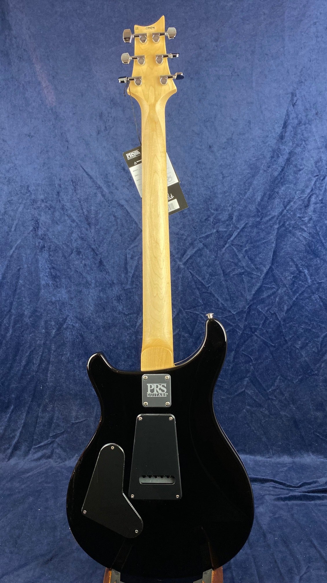 Black PRS electric guitar shown from the back, with natural wood neck, six tuning pegs, and two rear electronics covers on the body.