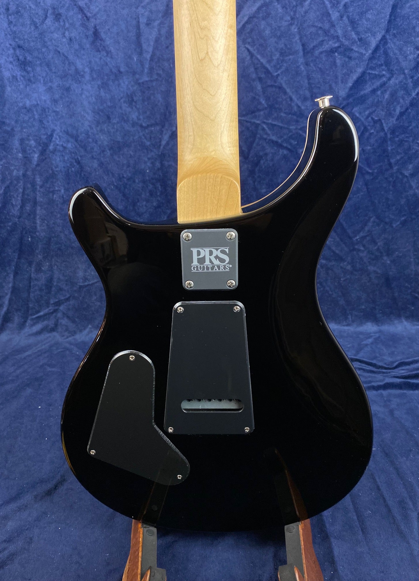 Black PRS electric guitar shown from the back with a natural wood neck and two black plastic cavity covers on the body.