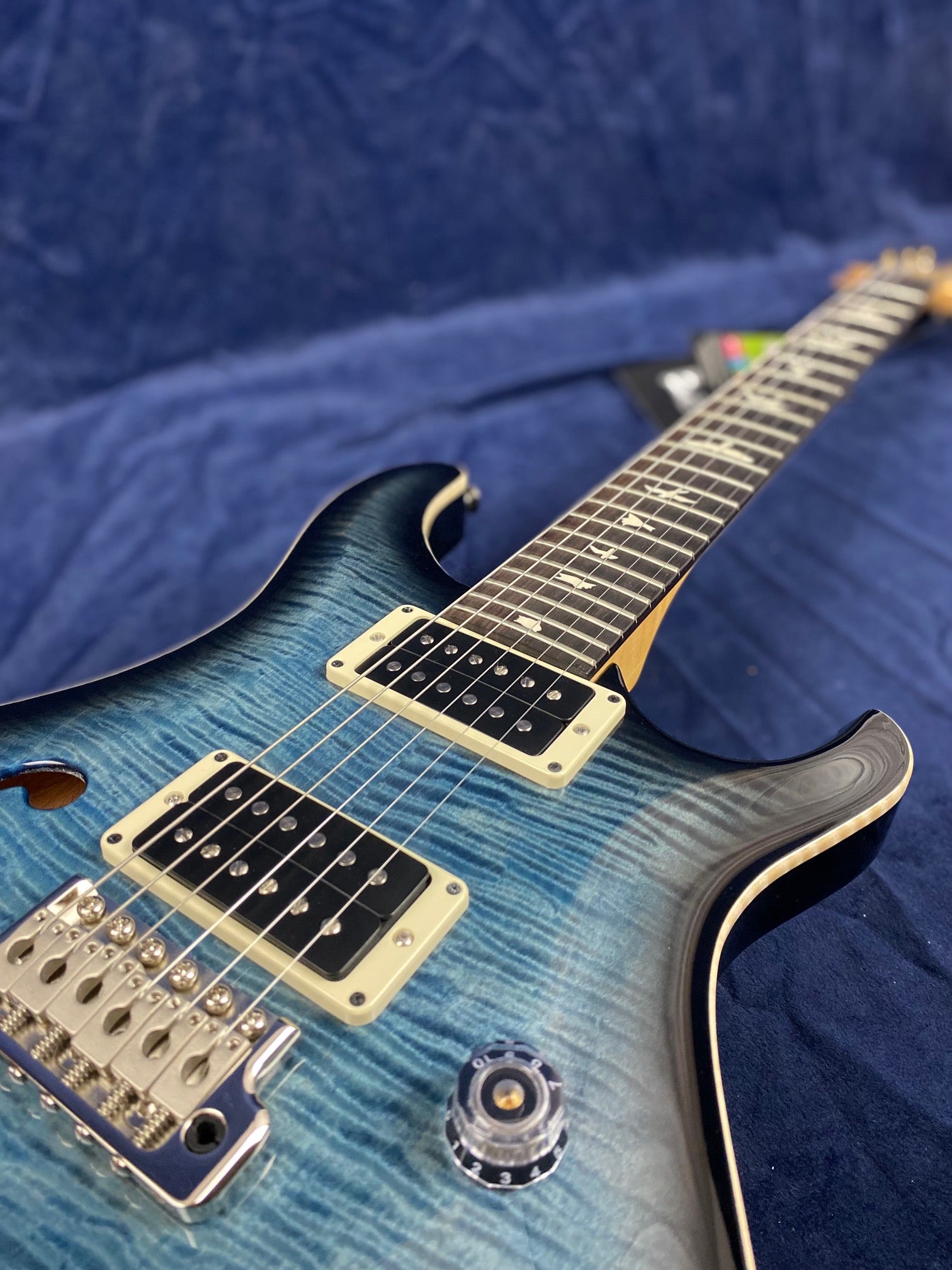 Blue electric guitar with a flamed maple top, two humbucker pickups, volume knob, and silver bridge, photographed on a blue fabric background.
