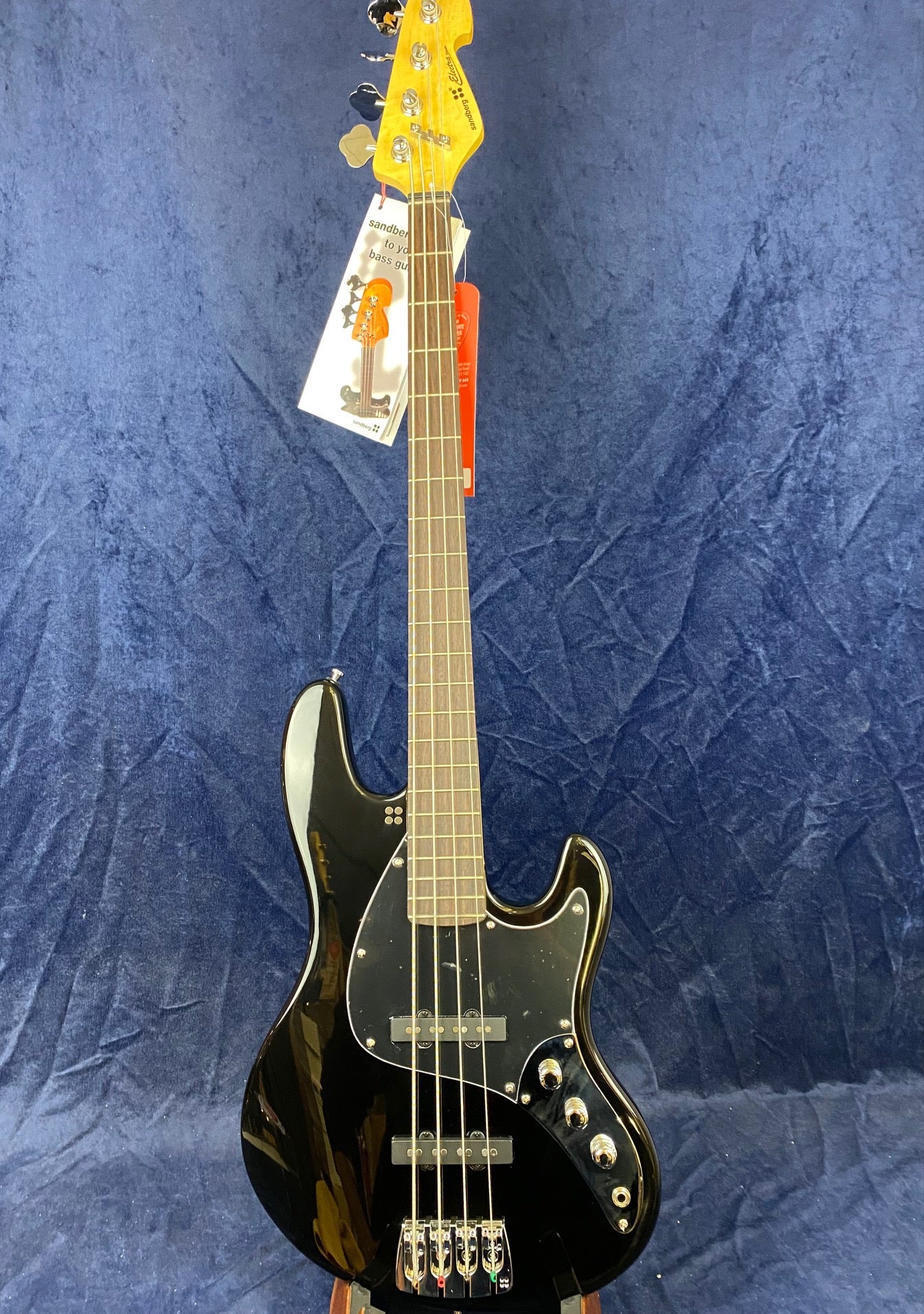 Black electric bass guitar with four strings, chrome hardware, black pickguard, and wooden neck against a dark blue textured fabric background.