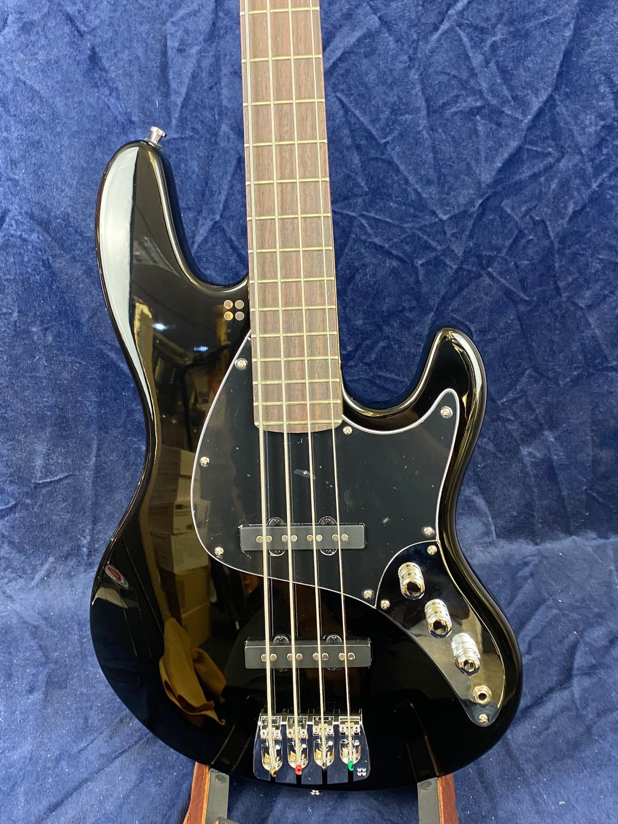 Glossy black electric bass guitar with four strings, chrome hardware, three control knobs, and a dark wood fretboard set against a blue background.