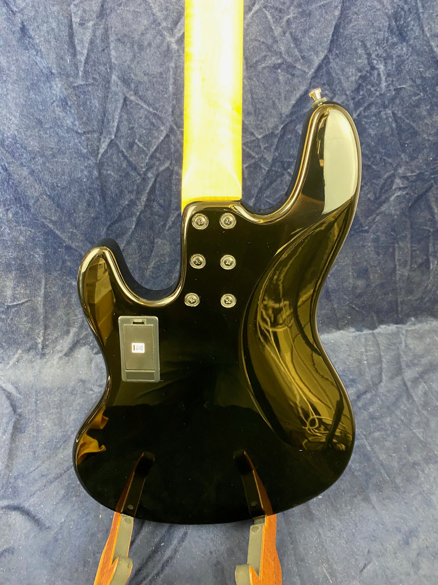 Glossy black electric bass back with a light wood neck, six screws at the neck joint, and a battery compartment on the body.