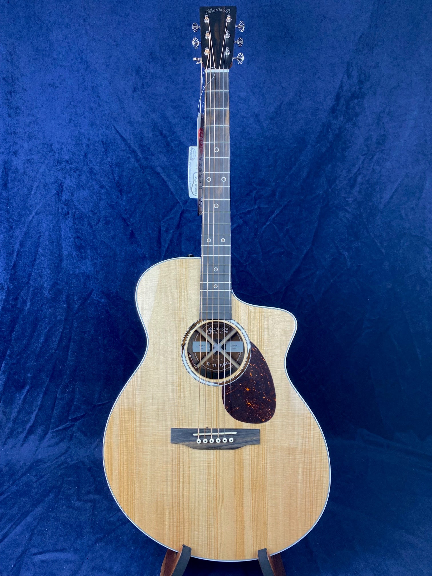 Natural wood Martin acoustic guitar with a round soundhole adorned by an X-brace pattern and a dark, teardrop-shaped pickguard on the right side.