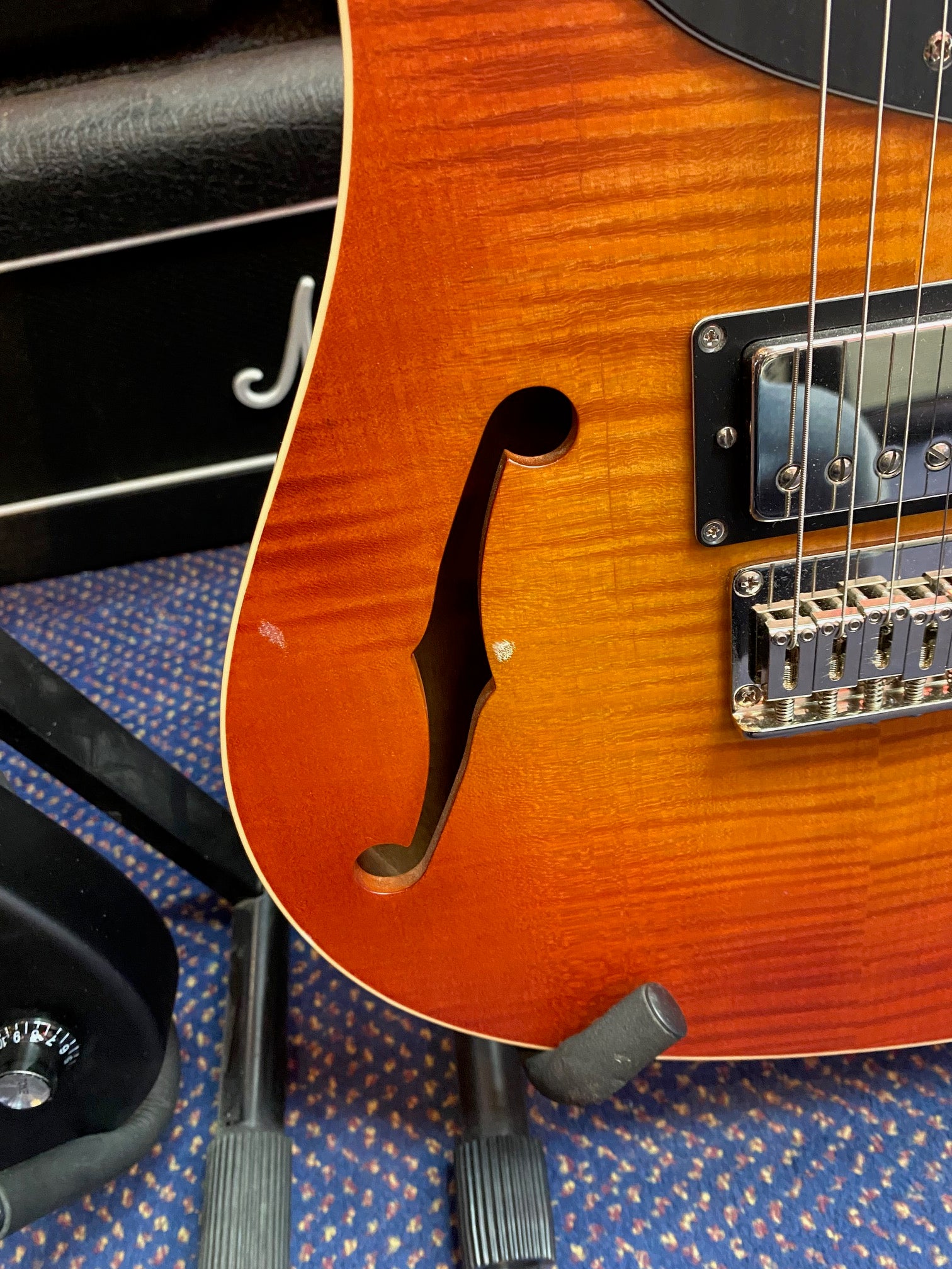 Sunburst electric guitar with a visible f-hole, chrome humbucker pickup, and minor dings on the body’s edge, resting on a stand.