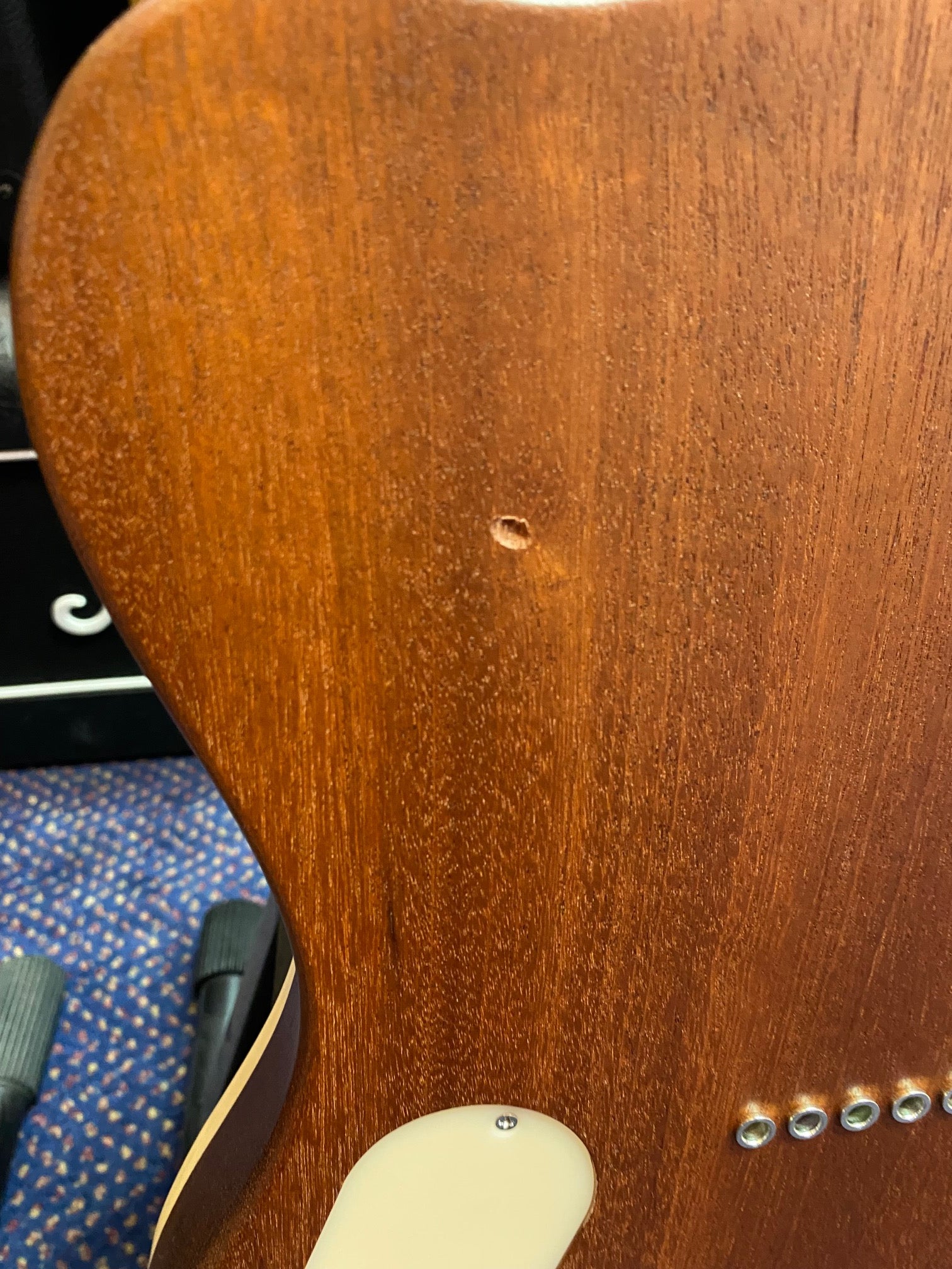 Back of an electric guitar with a natural wood finish, showing a small dent near the center and part of the plastic cover for electronics.