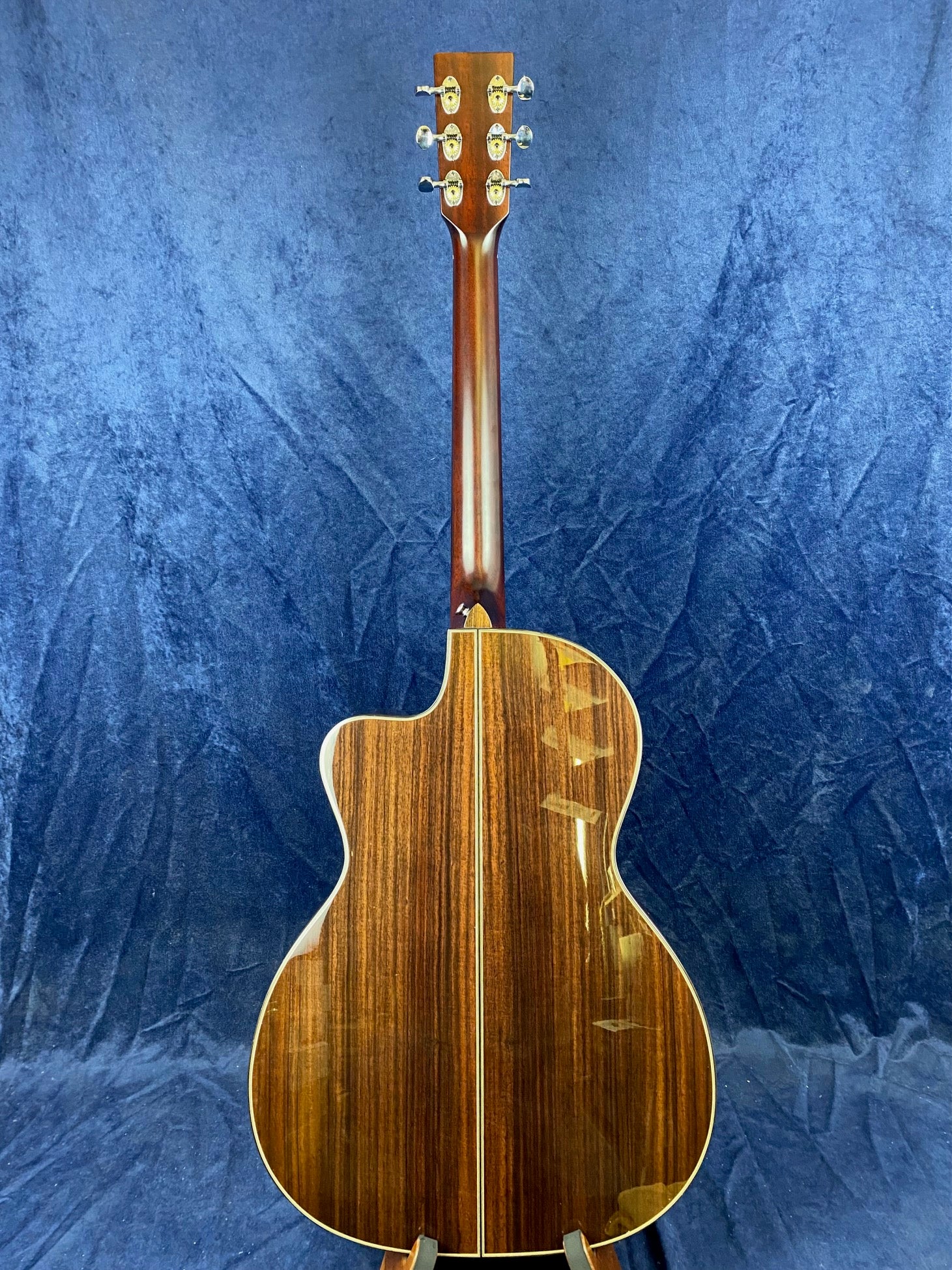 Glossy wood acoustic guitar back and neck, deep brown color with lighter vertical grain lines, gold tuning pegs, single cutaway body shape.
