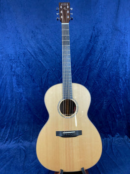 Light wood Auden acoustic guitar with six strings, dark wood fretboard, and round soundhole, displayed upright against a blue textured background.