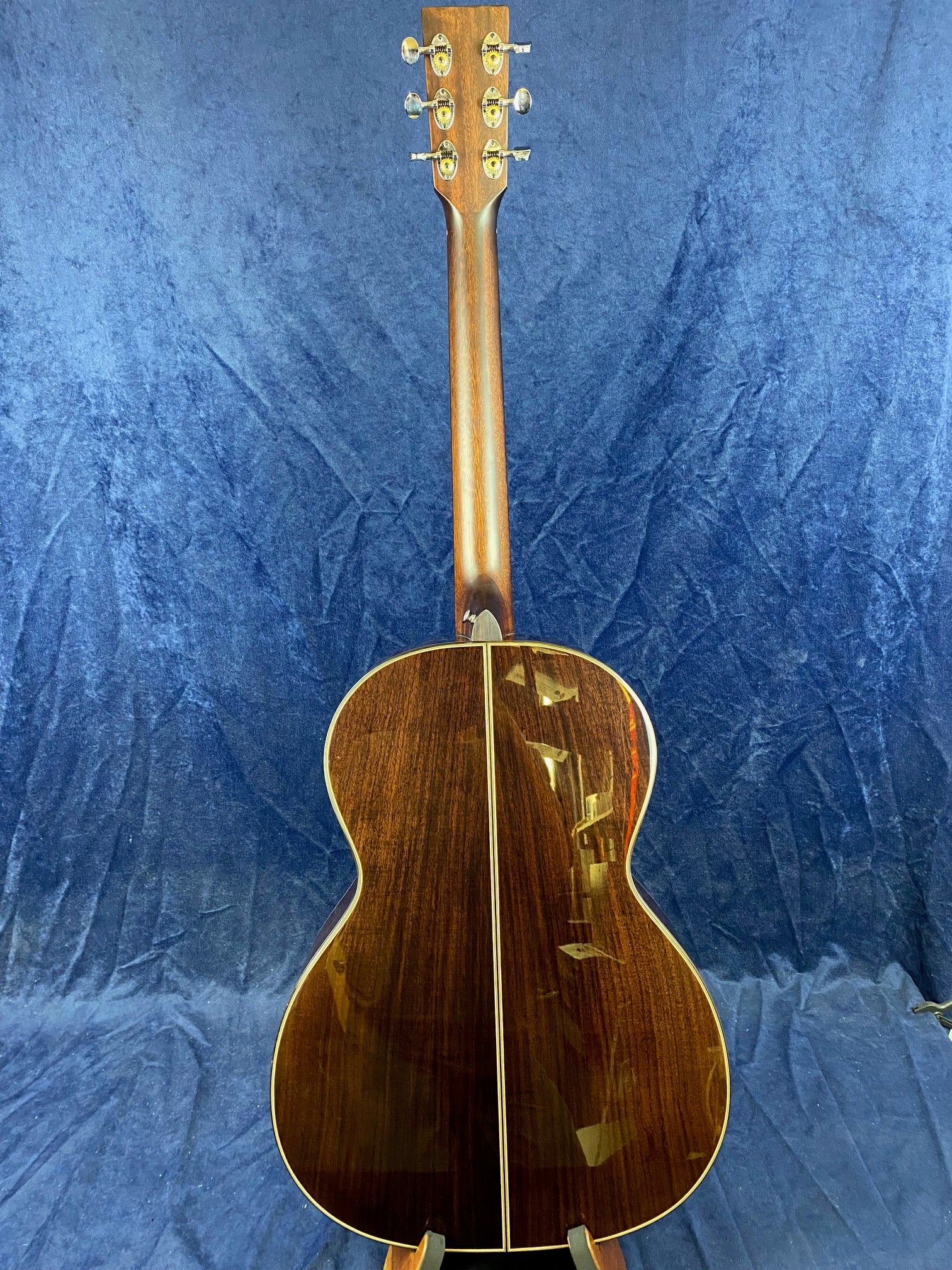 Acoustic guitar shown from the back with a dark, glossy wooden finish and a straight lighter wood inlay running down the center.