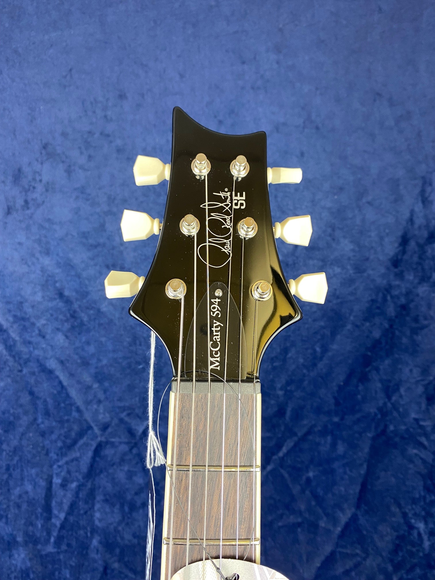 PRS SE electric guitar headstock with cream tuning pegs, six strings, and “McCarty 594” plus signature printed on the black surface.