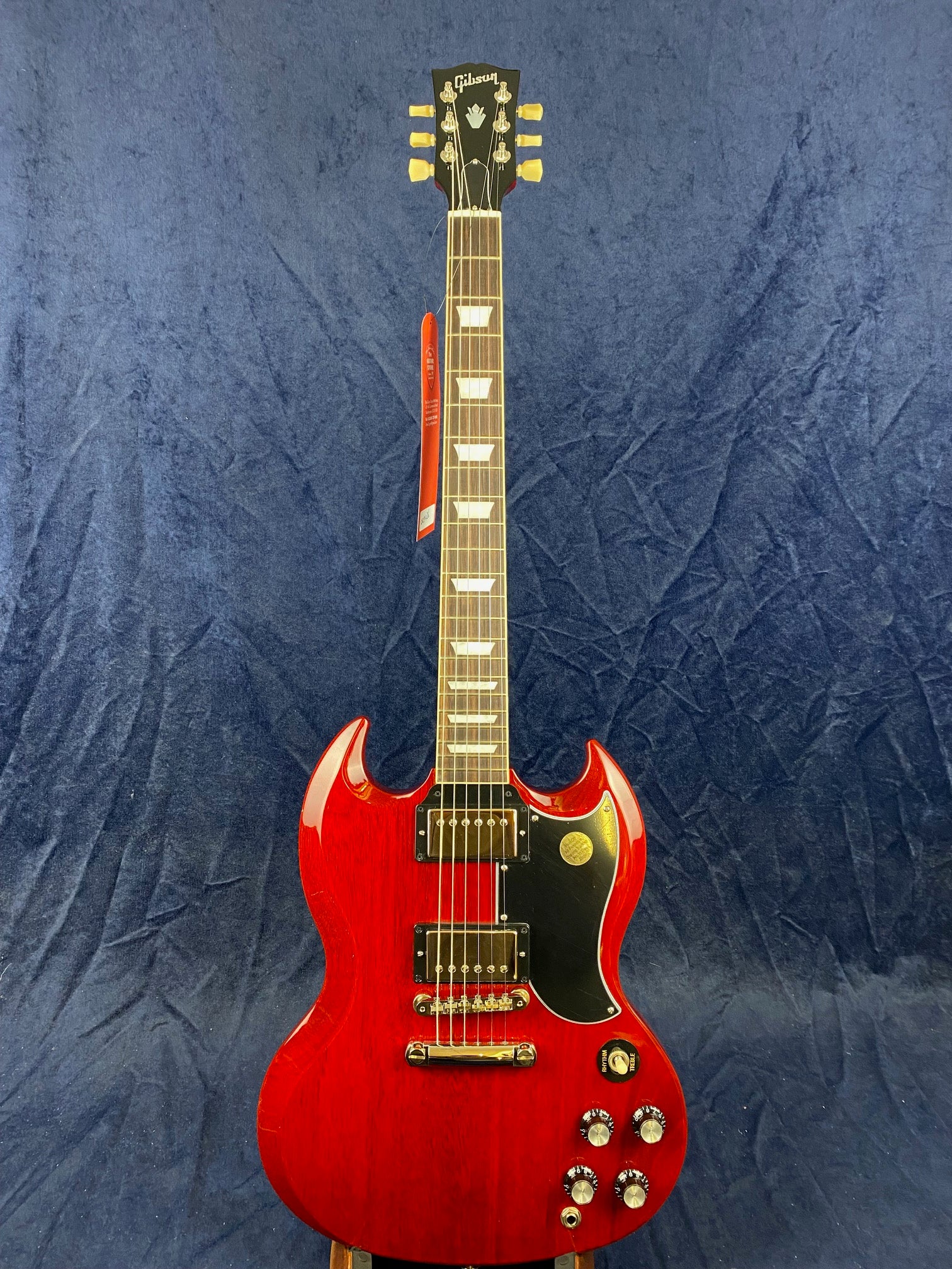 Cherry red electric guitar with a double-cutaway body, black pickguard, two humbucker pickups, four control knobs, and trapezoid inlays on the neck.