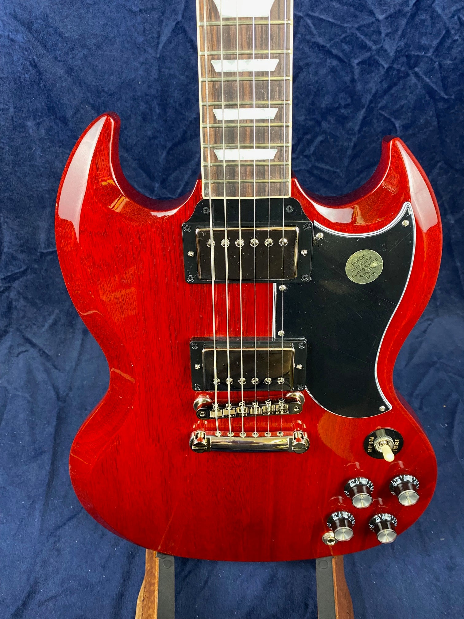 Cherry red electric guitar with two humbucker pickups, black pickguard, four control knobs, and a toggle switch on a dark blue background.