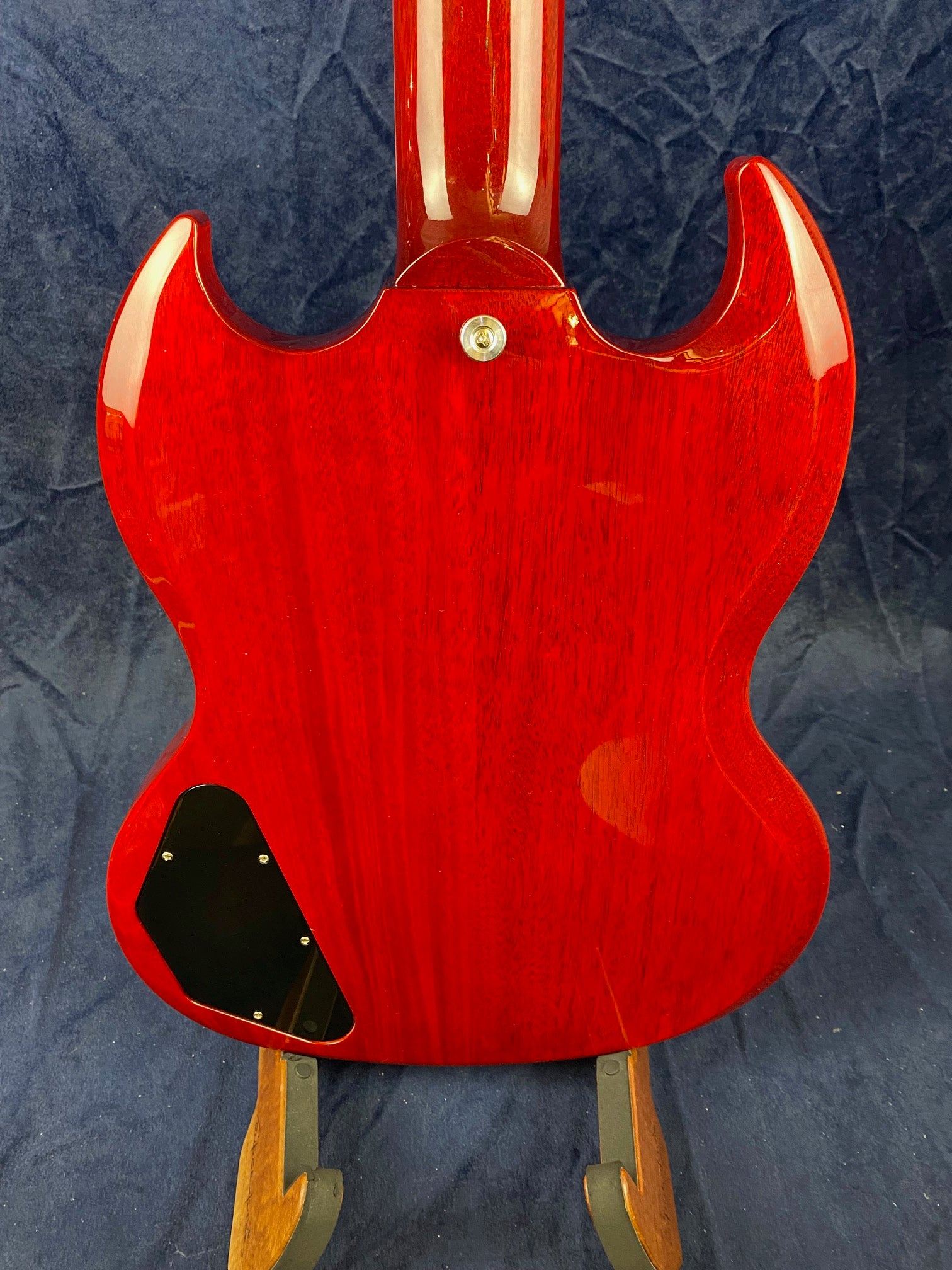 Glossy red electric guitar back with two pointed horns, a central neck join, black control cavity cover, and visible wood grain.