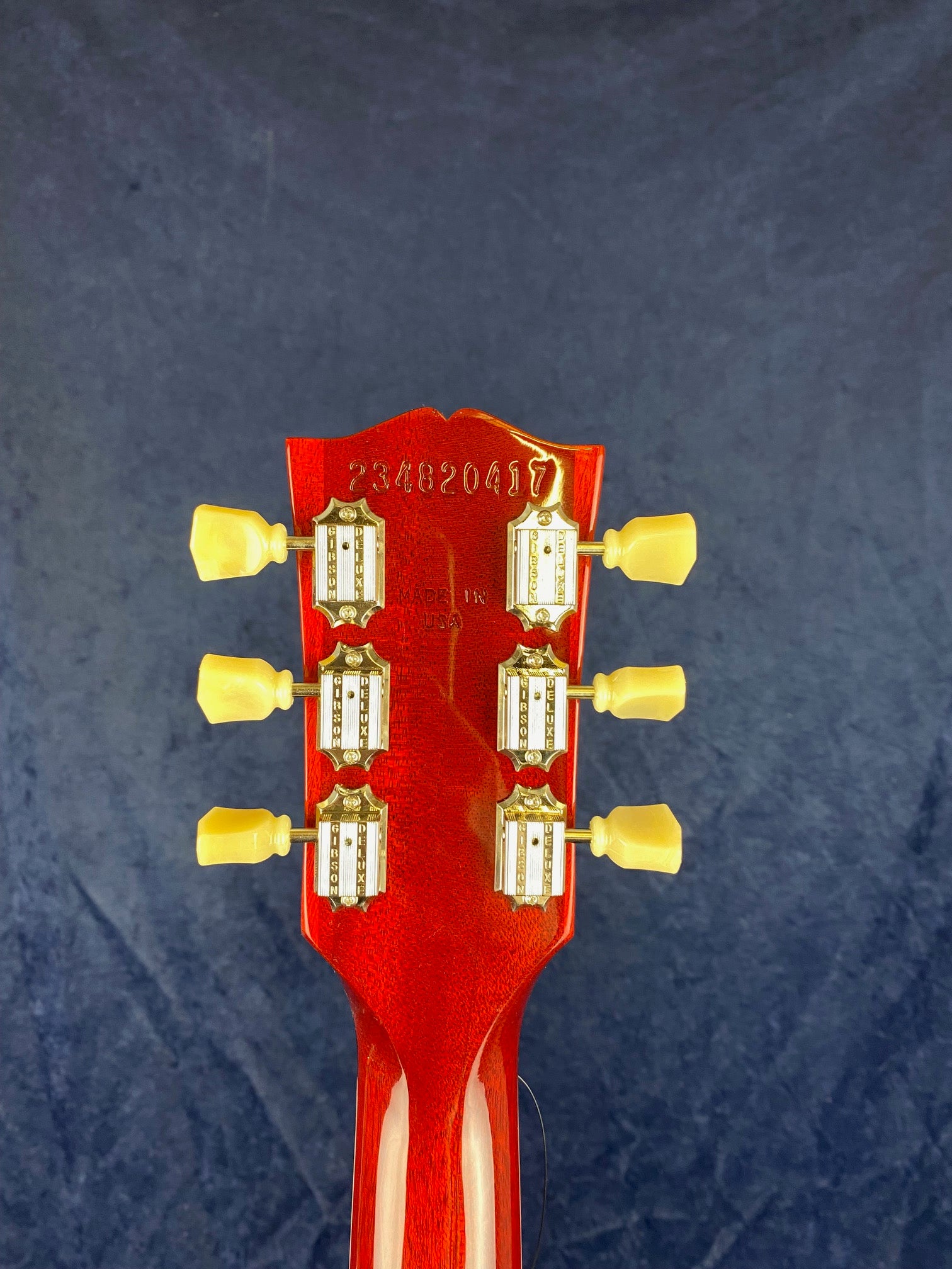 Back of a red electric guitar headstock with six cream tuning pegs and "Made in USA" plus a serial number stamped above.