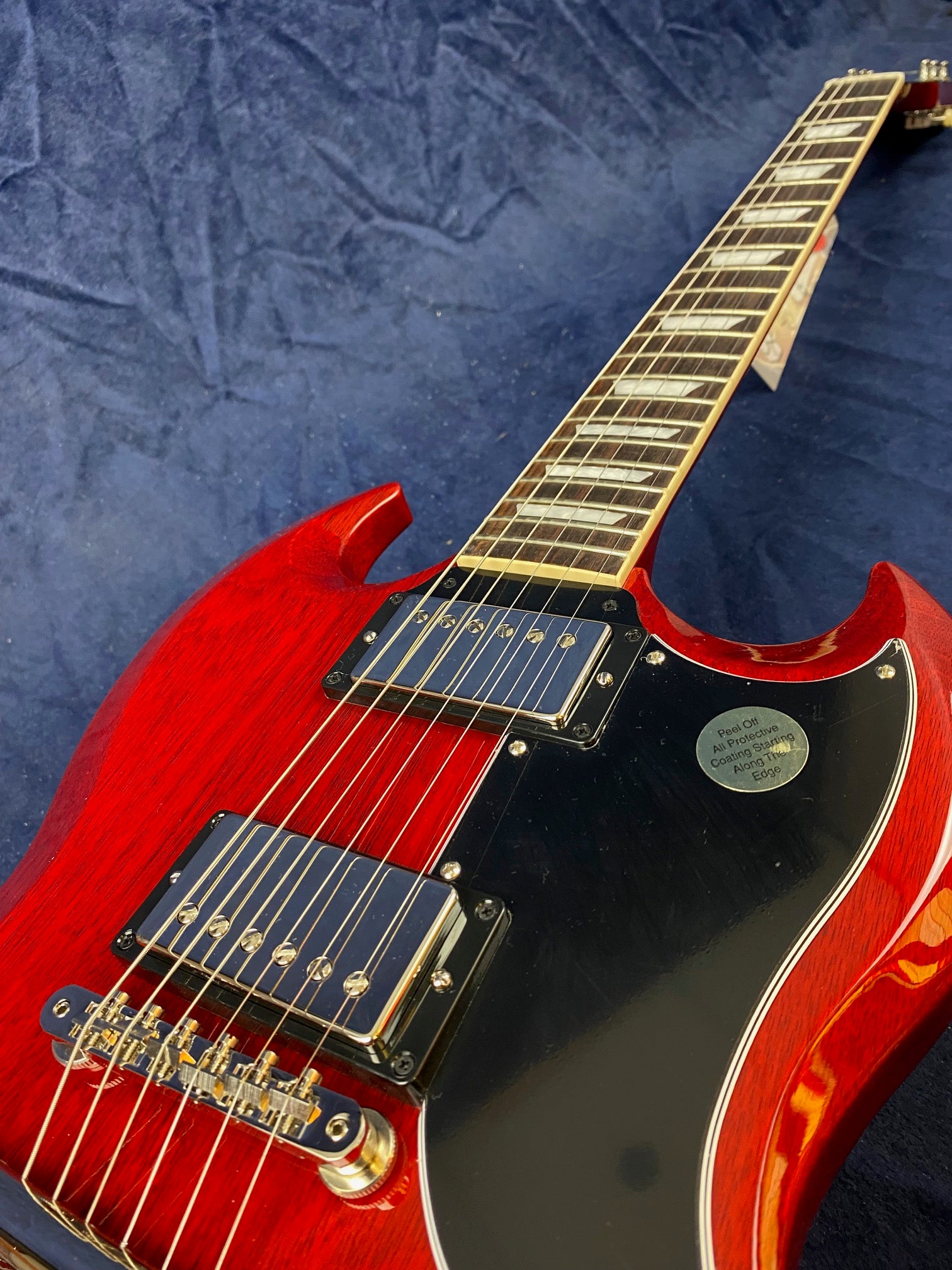 Cherry red electric guitar with a black pickguard, chrome pickups, and dual cutaway body, lying on a textured dark blue surface.