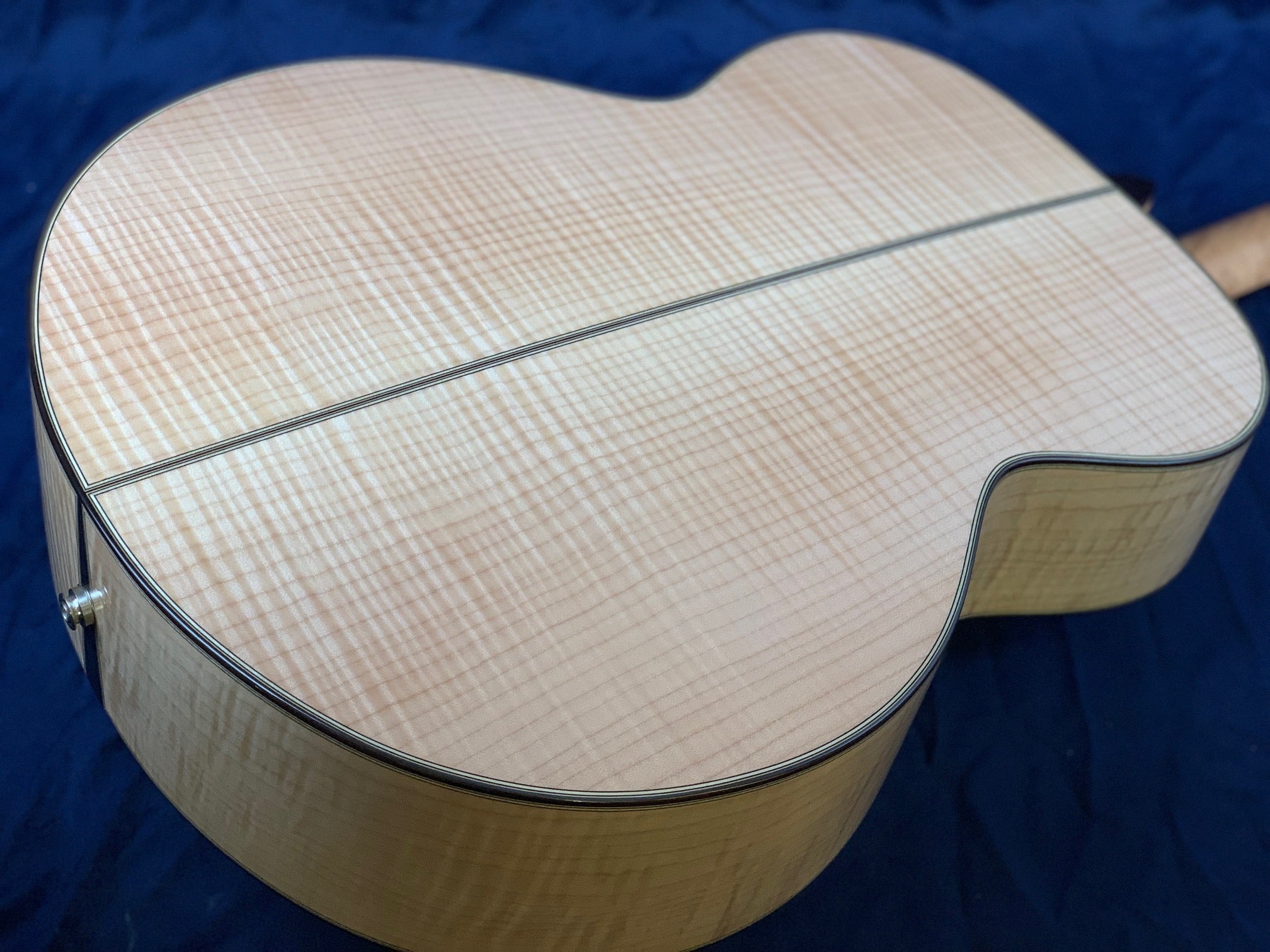 Acoustic guitar back made of light-colored, highly figured maple wood with a visible central seam and dark binding around the edges.