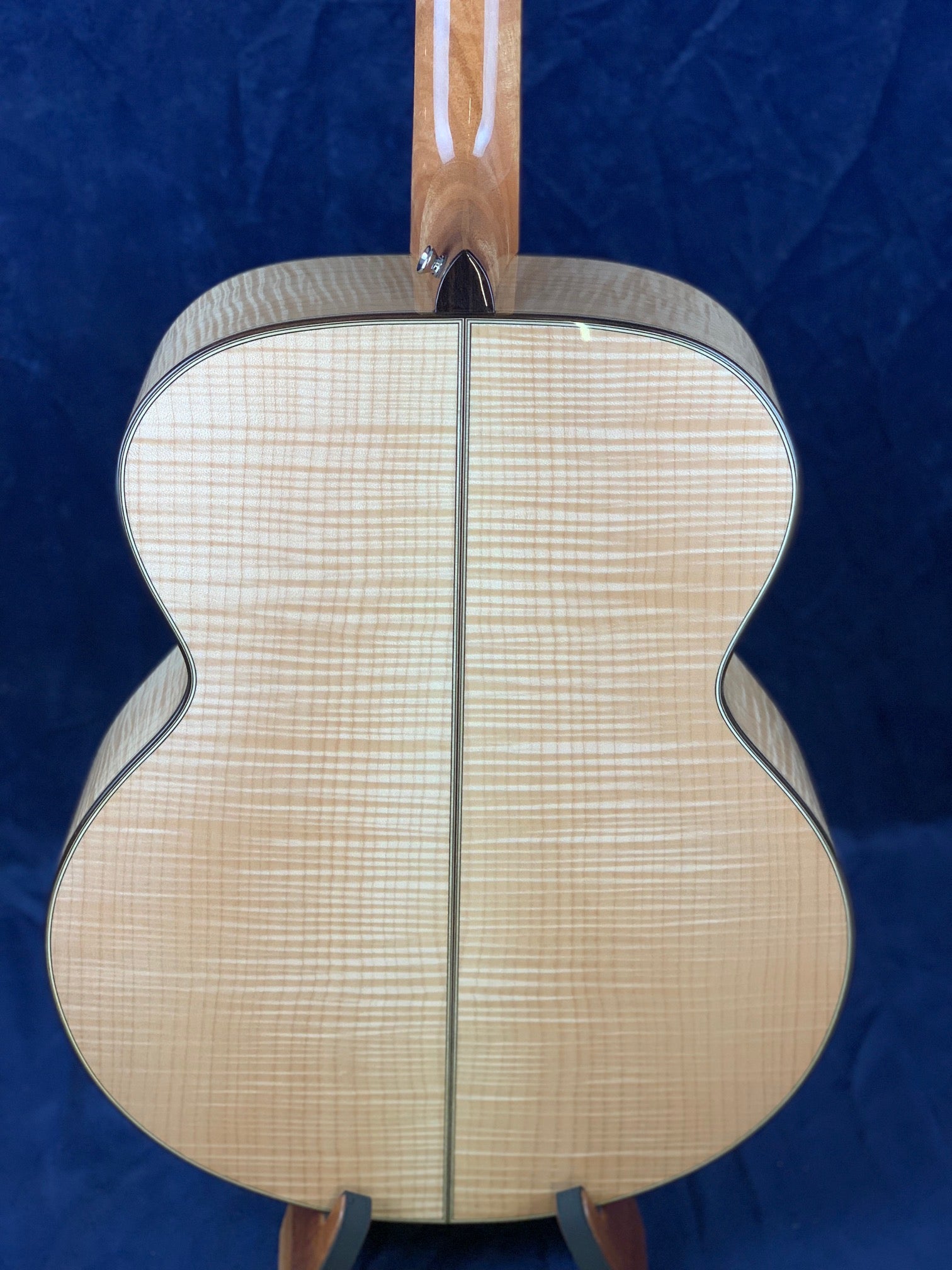 Curly maple wood acoustic guitar back with light natural finish, vertical center seam, and subtle striping grain pattern.