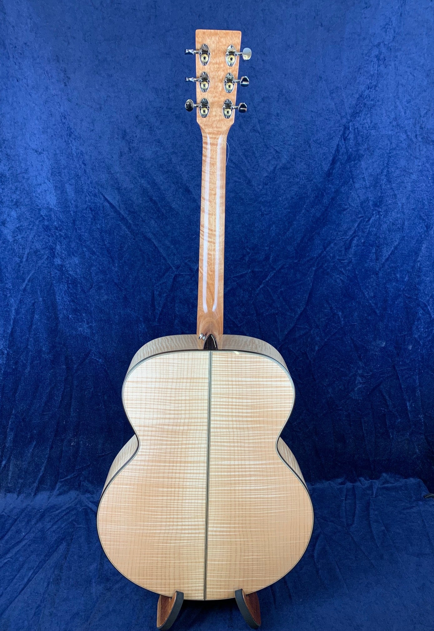 Curly maple back acoustic guitar with a striped wood pattern, viewed from behind, featuring six tuning pegs and a natural wood finish.