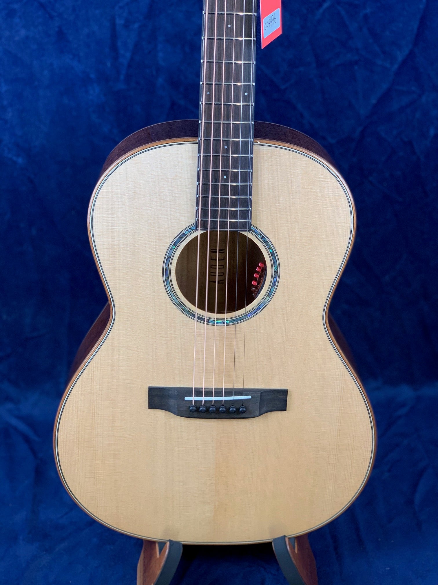 Acoustic guitar with a light wood top, dark wood sides, round sound hole, six strings, and a black bridge, set against a dark blue background.