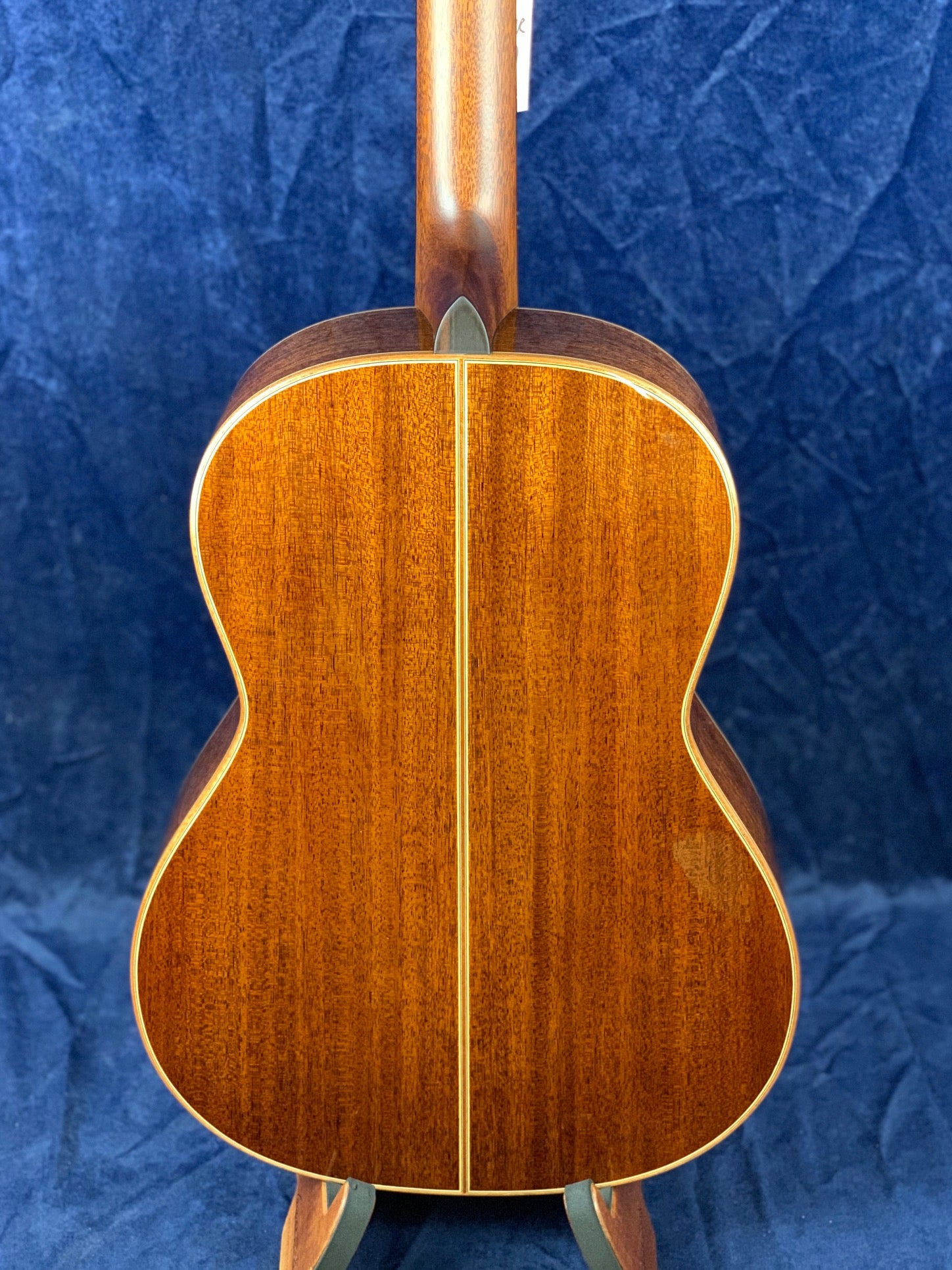 Warm brown acoustic guitar back with a center seam and light trim, shown against a dark blue textured background.