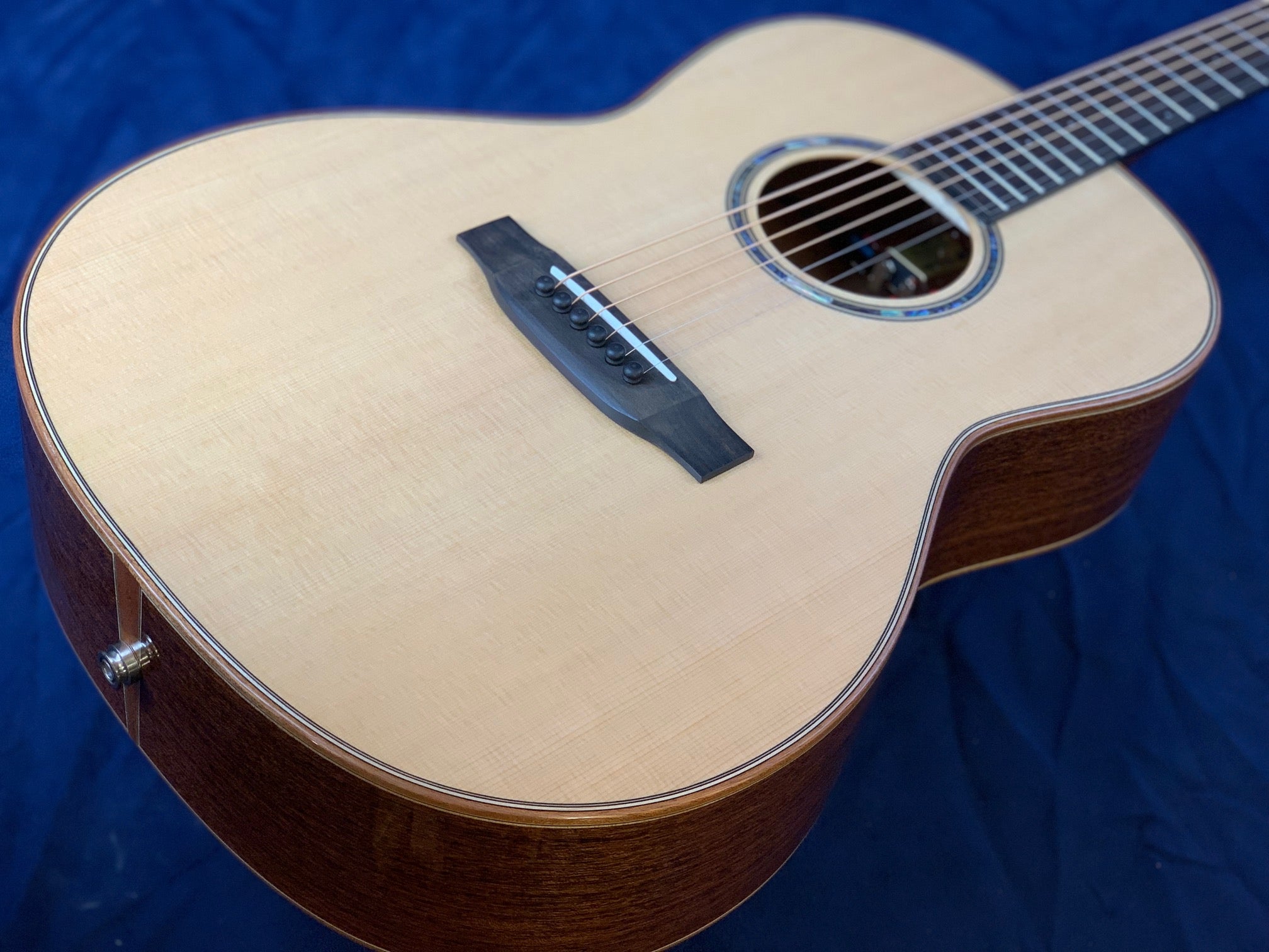 Acoustic guitar with a light wood top, dark wooden sides, six strings, and decorative ring around the sound hole, lying on a dark fabric background.