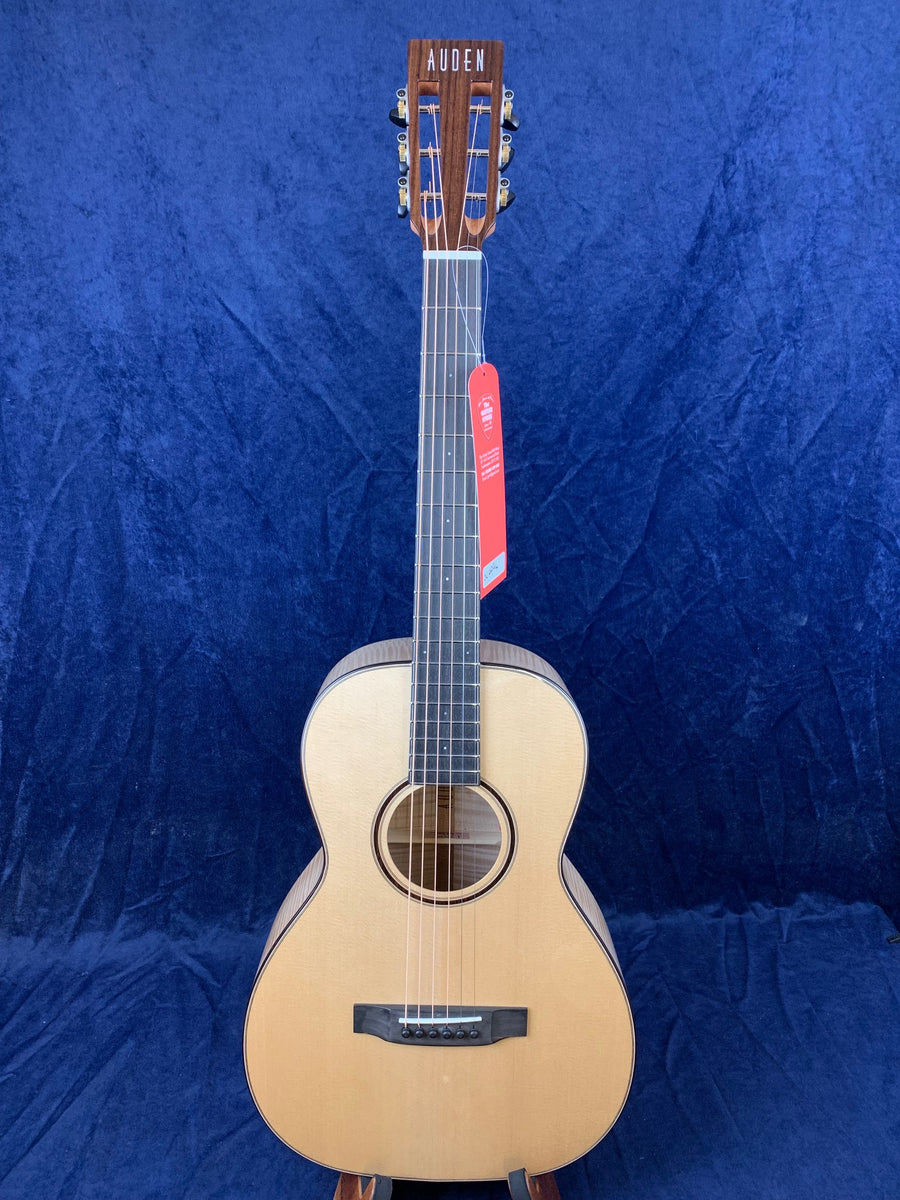 Auden acoustic guitar with a light wood body, dark wood bridge and headstock, six strings, and a red tag hanging from the tuning pegs.