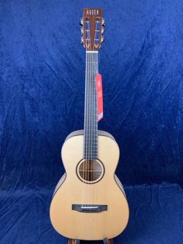 Auden acoustic guitar with a light wood body, dark wood bridge and headstock, six strings, and a red tag hanging from the tuning pegs.