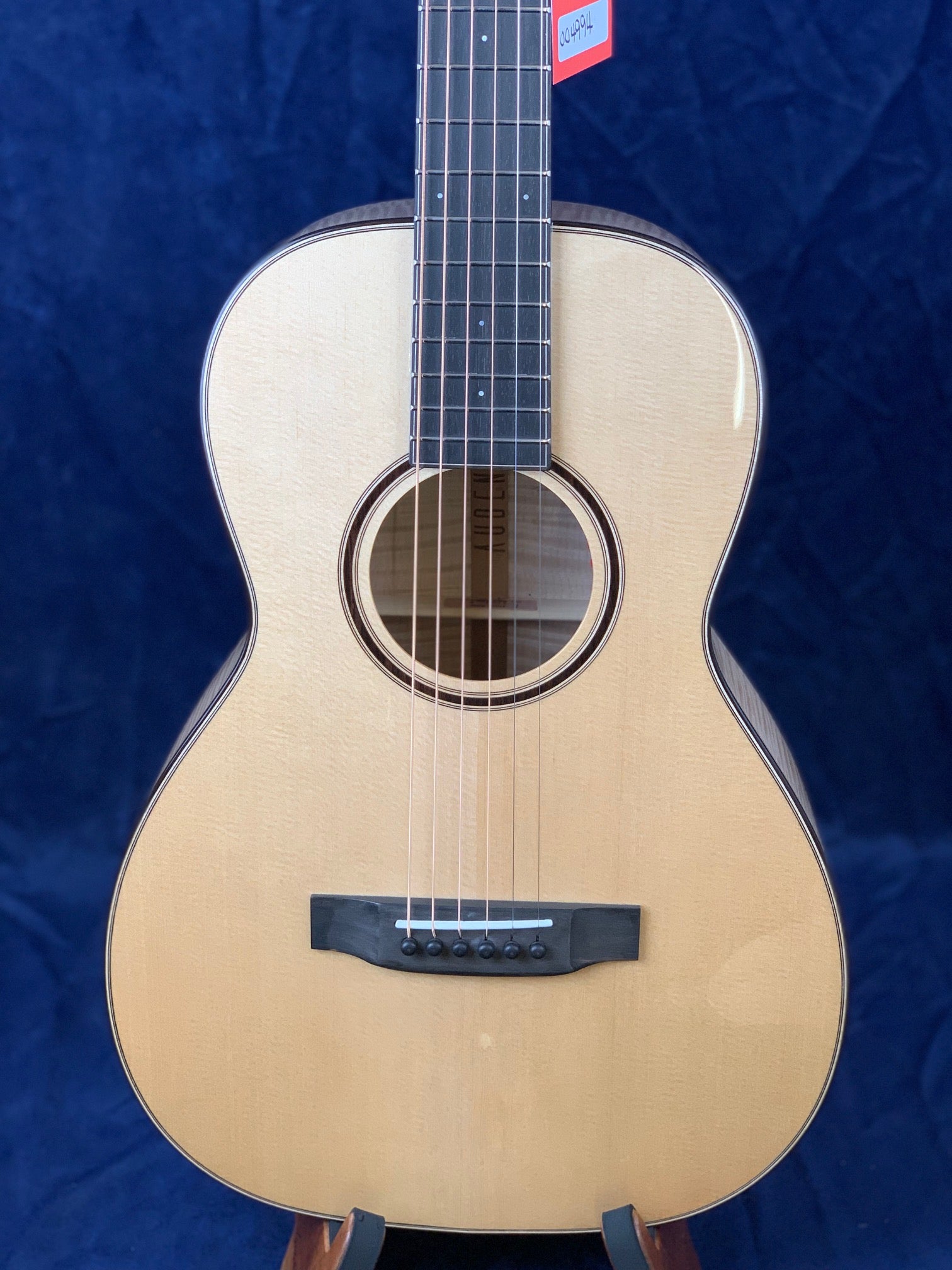 Light wood acoustic guitar with a dark bridge, six strings, and a circular sound hole on a stand, set against a dark blue background.