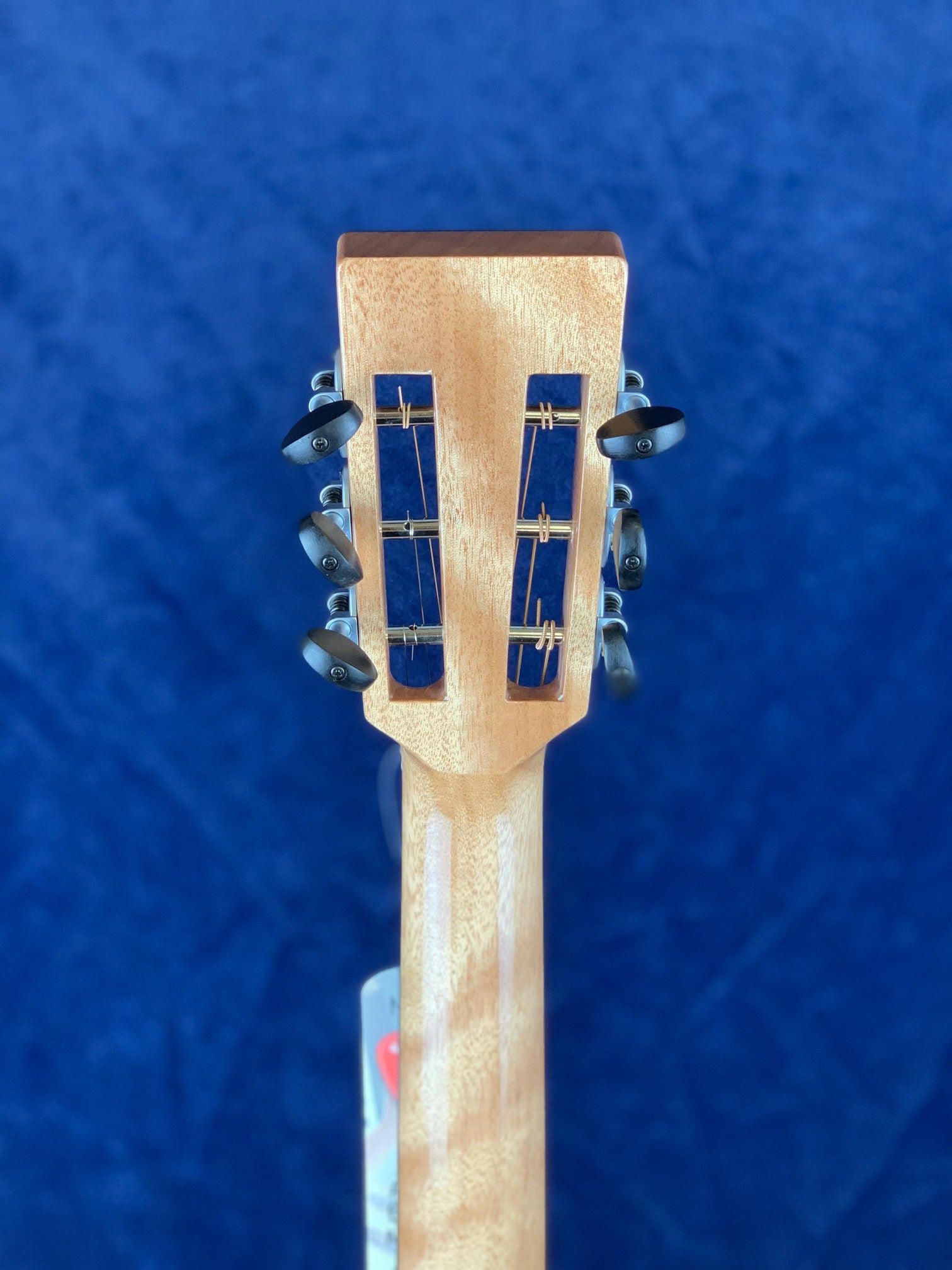 Acoustic guitar headstock viewed from the back, showing six black tuning pegs, two vertical slotted openings, and a light wood finish.