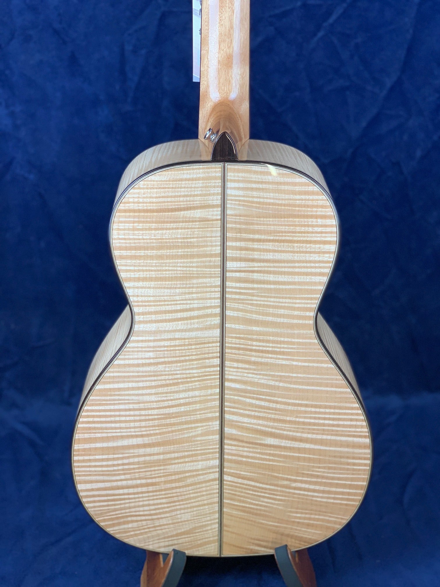 The back of an acoustic guitar made from light-colored wood with striking horizontal flame-like stripes and a thin dark center seam.