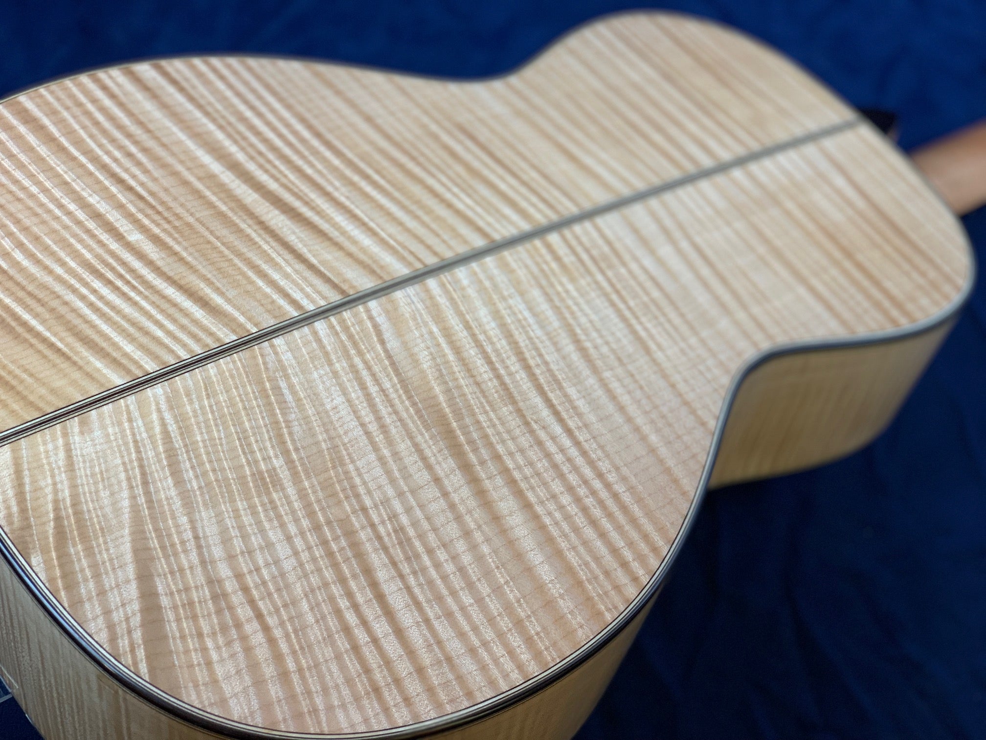 Back of an acoustic guitar with glossy light wood and striking wavy grain patterns, divided by a thin dark center line.
