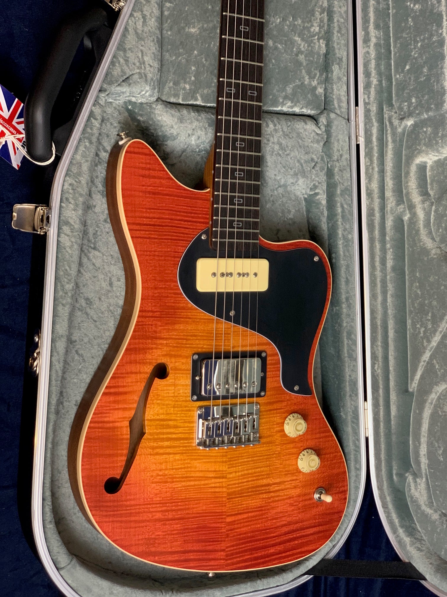 Electric guitar with a vibrant orange sunburst finish, single f-hole, two pickups, black pickguard, two control knobs, and a selector switch in a hard case.