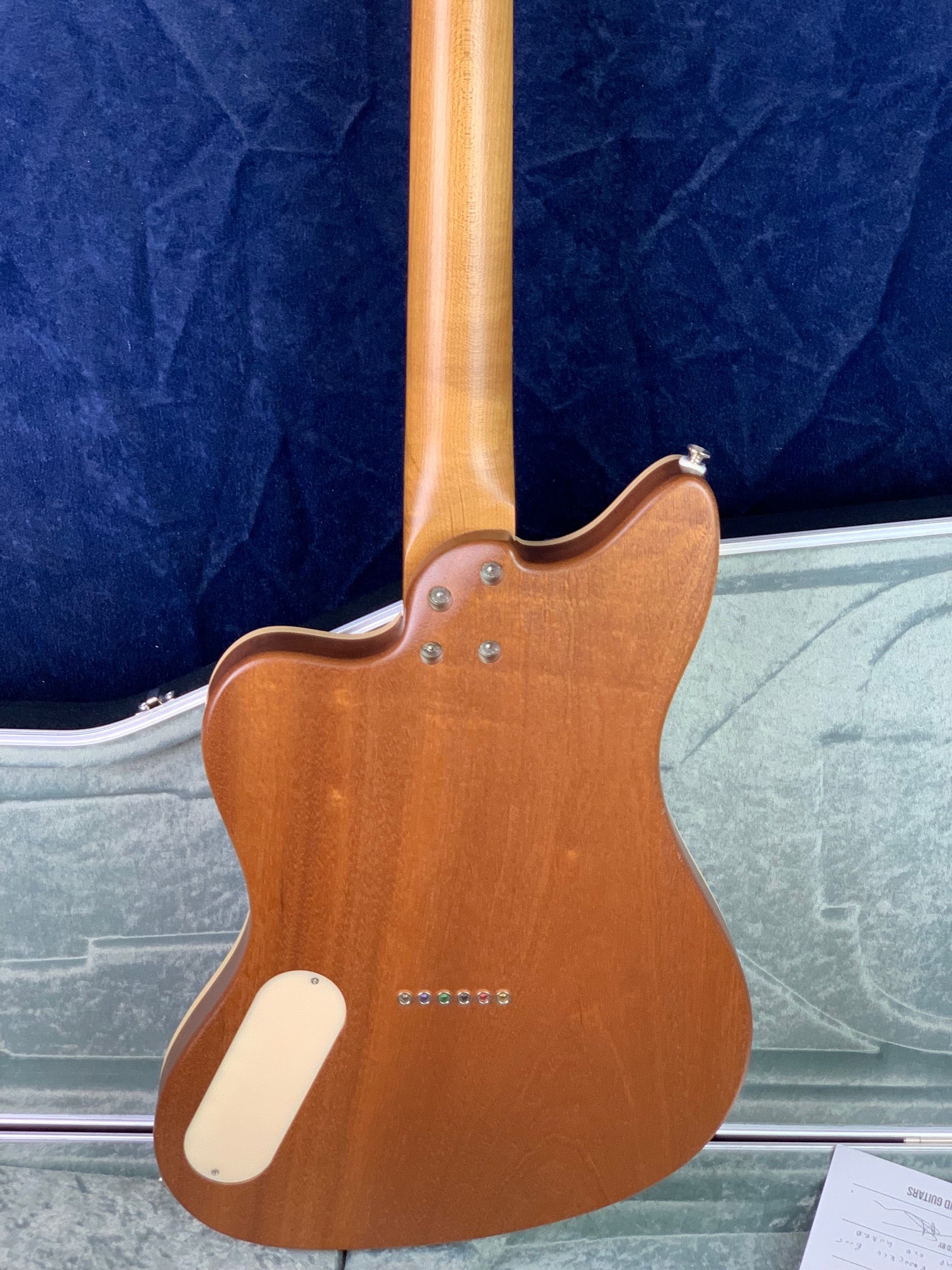 Back view of an electric guitar with a natural wood finish, six string-through ferrules, contoured neck joint, and an off-white electronics cover.