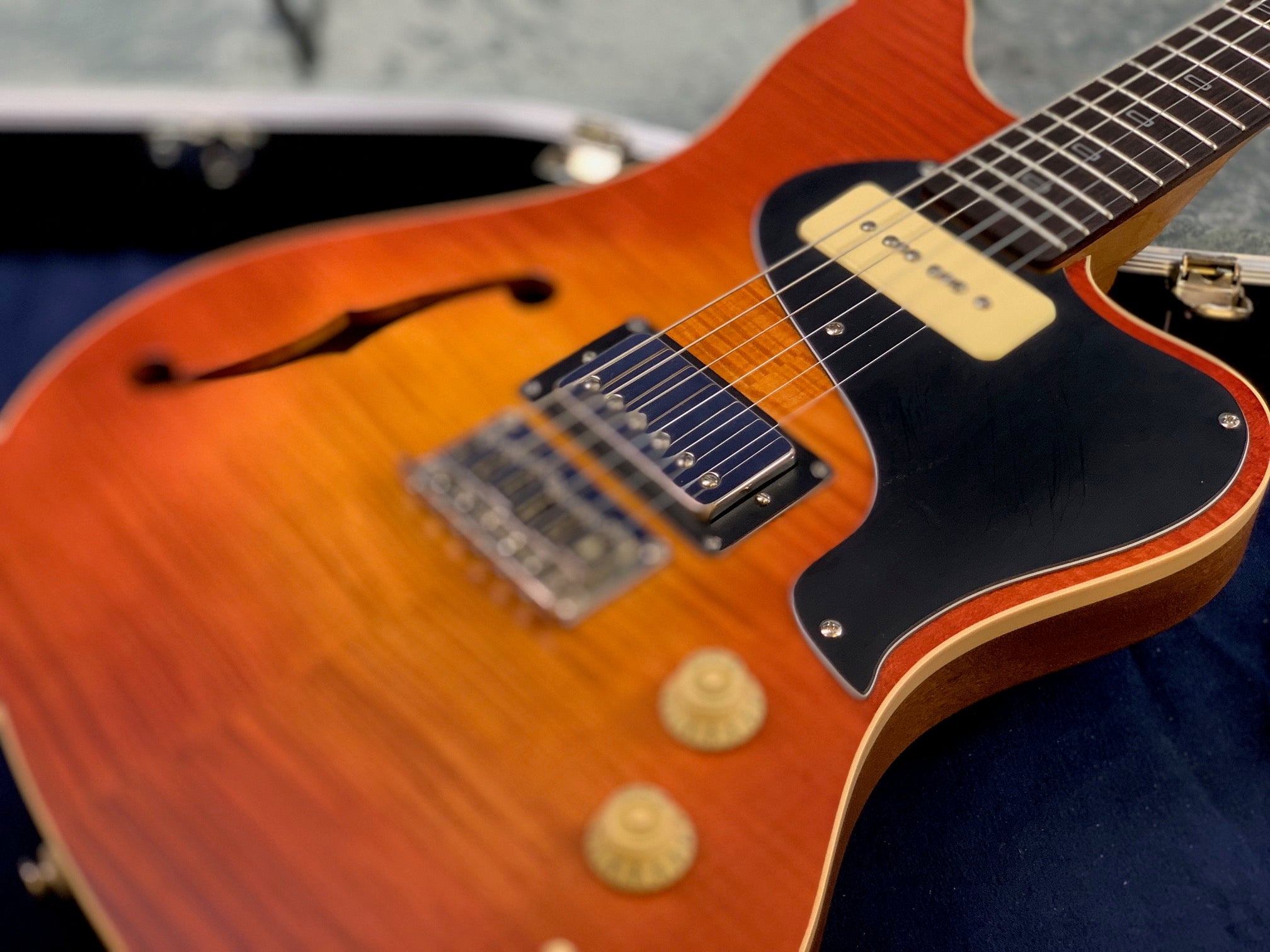 Sunburst electric guitar with a semi-hollow body, two pickups, black pickguard, two gold control knobs, and an f-hole on the left side.