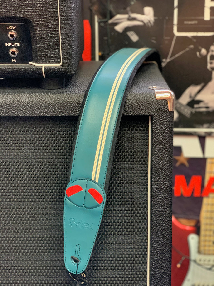 Teal guitar strap with two white stripes and red accents draped over a black textured amplifier.