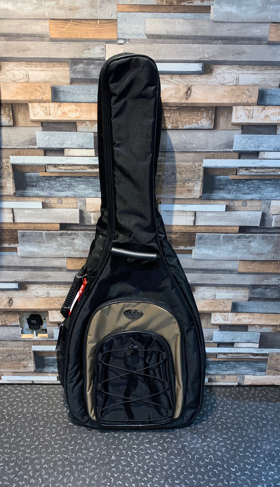 Black and olive soft guitar case standing upright, featuring a handle, front zipper pocket, and bungee cord storage on the pocket.