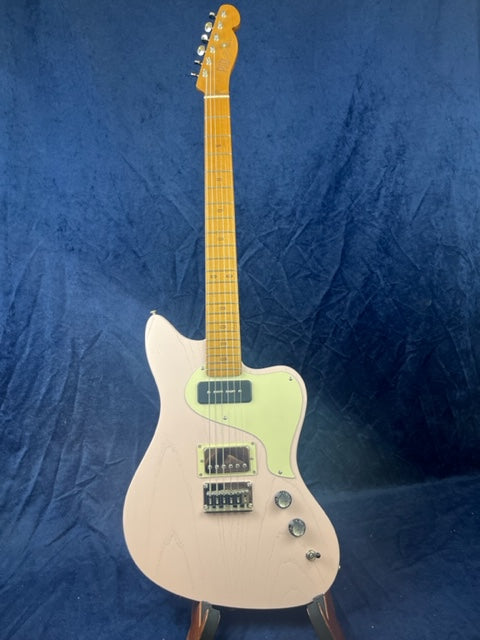 Pale pink electric guitar with a maple neck, two black pickups, three control knobs, and a light green pickguard, set against a dark blue background.