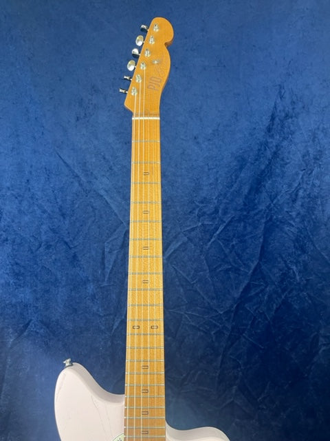 Light-colored electric guitar neck and partial body against a blue background, six tuning pegs visible on the headstock.