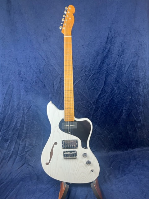 White electric guitar with a black pickguard, two pickups, semi-hollow body featuring an f-hole, and a maple neck, shown upright against a blue background.
