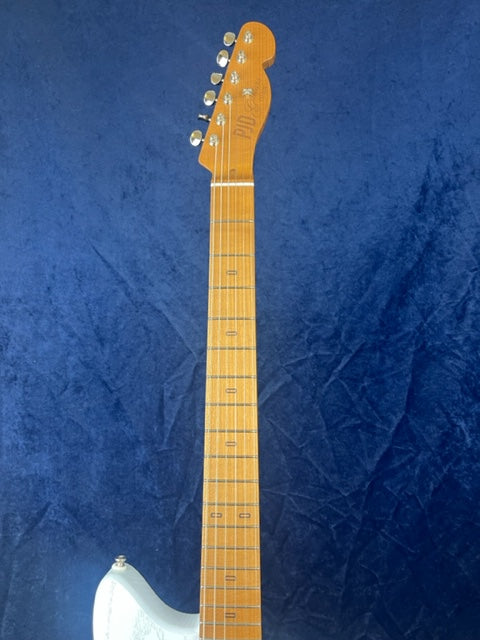 Electric guitar with a light brown neck and headstock, six tuning pegs, and part of a white guitar body, set against a dark blue background.